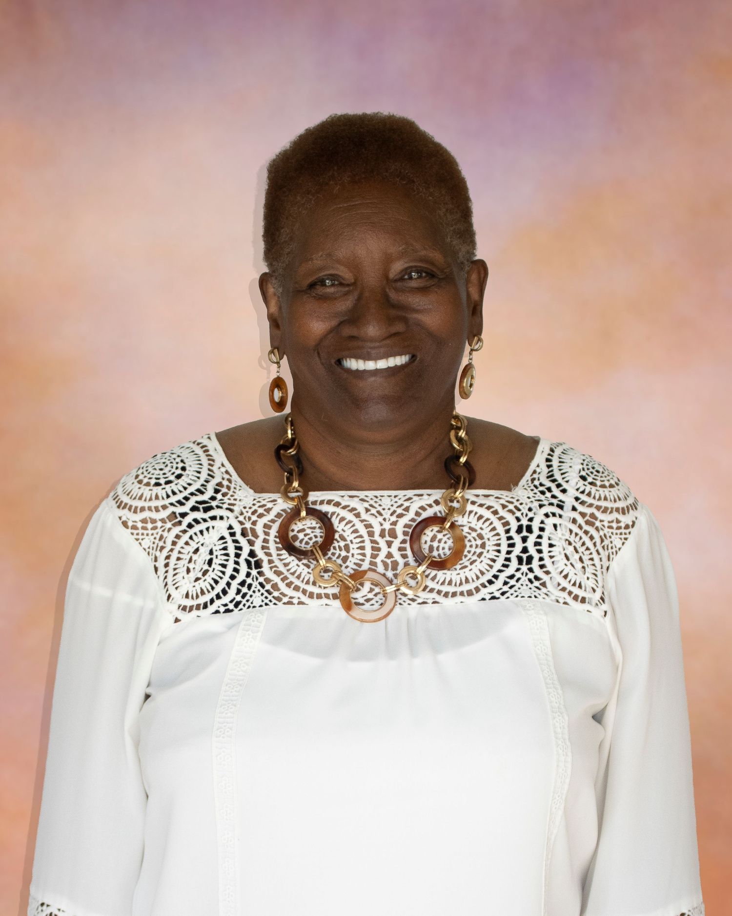 Smiling woman in white crochet top with gold jewelry posing for a portrait photo.