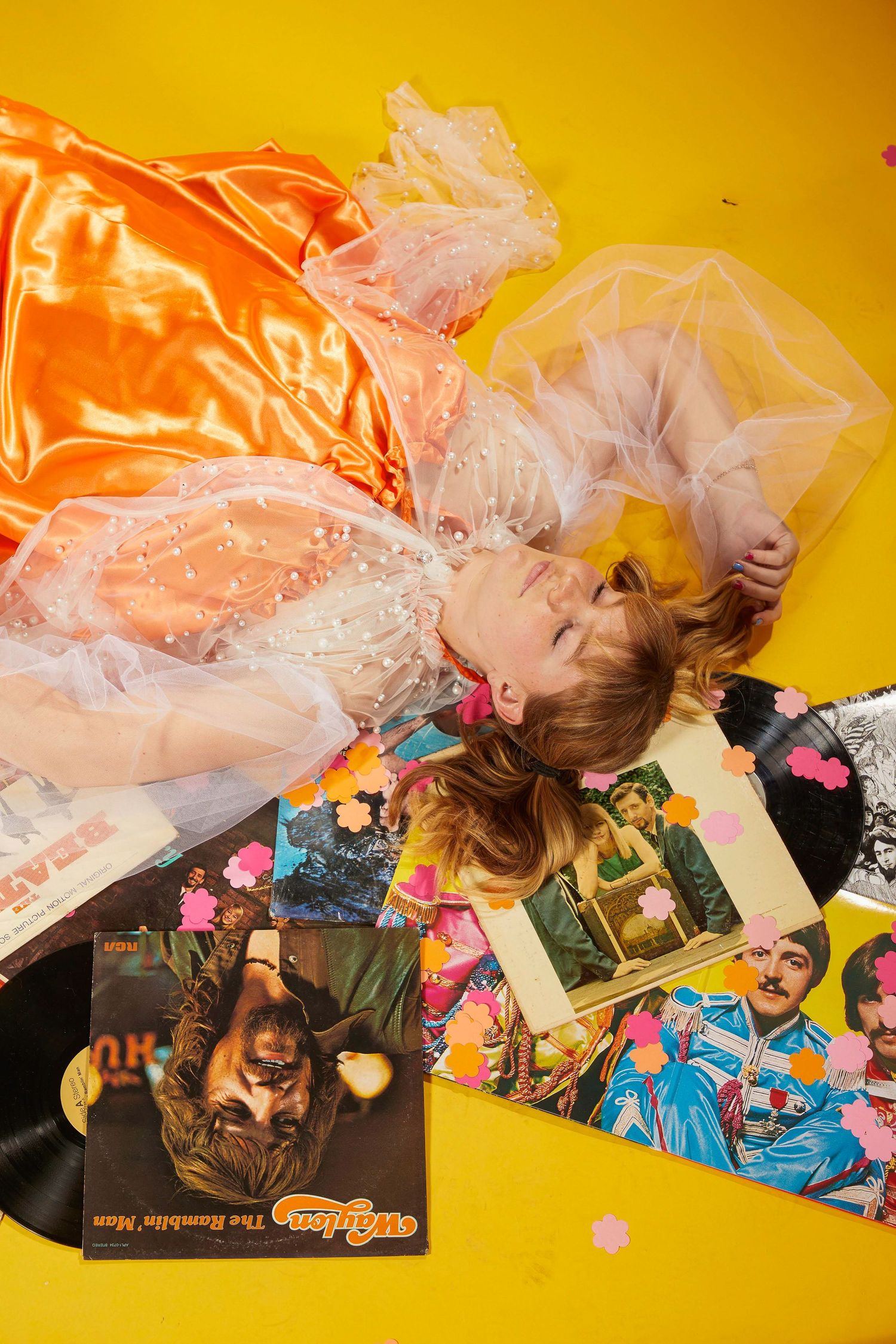 Person lying on yellow background surrounded by scattered photographs and tulle fabric.