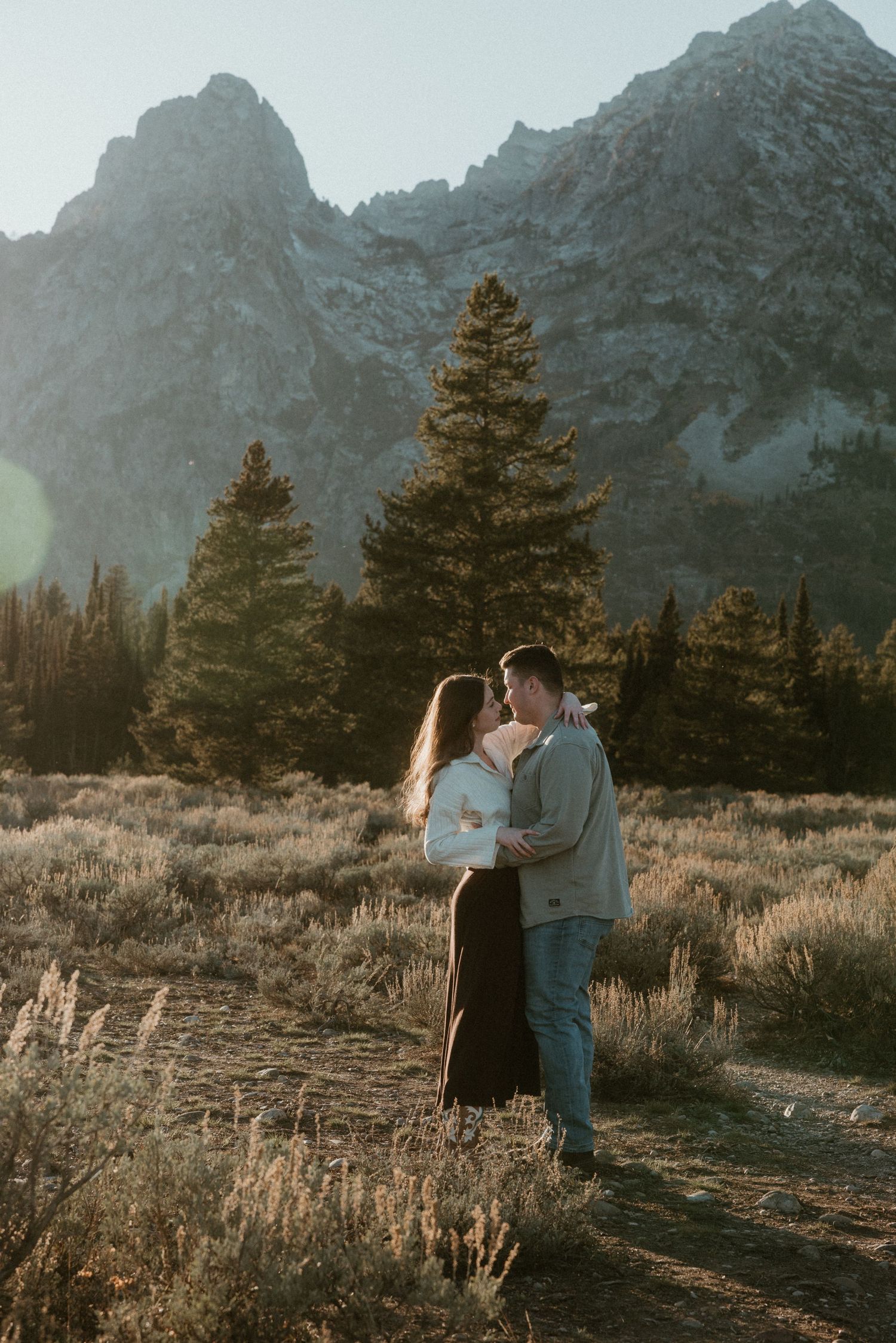 A couple shares an intimate moment against a backdrop of snow-capped mountains and evergreen trees.