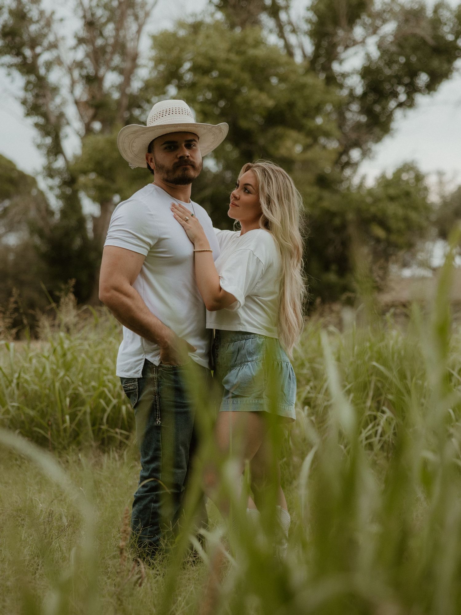 Romantic couple embracing in tall grass field during golden hour photoshoot.
