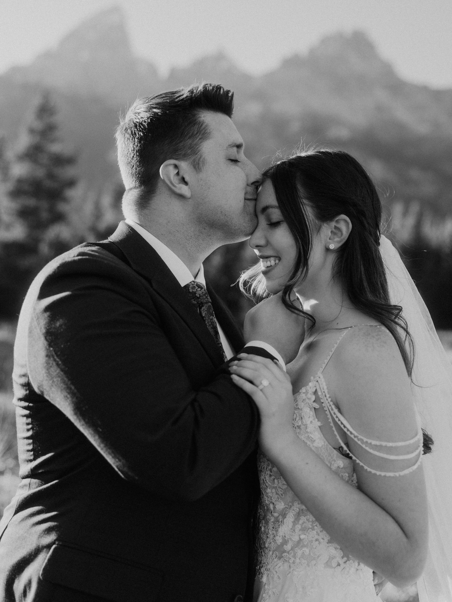 Black and white portrait of newlyweds sharing romantic kiss outdoors.