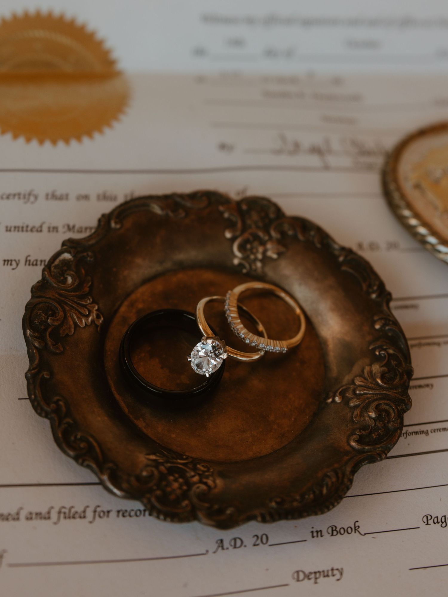 Wedding rings displayed on an ornate vintage brown dish against a marriage certificate.