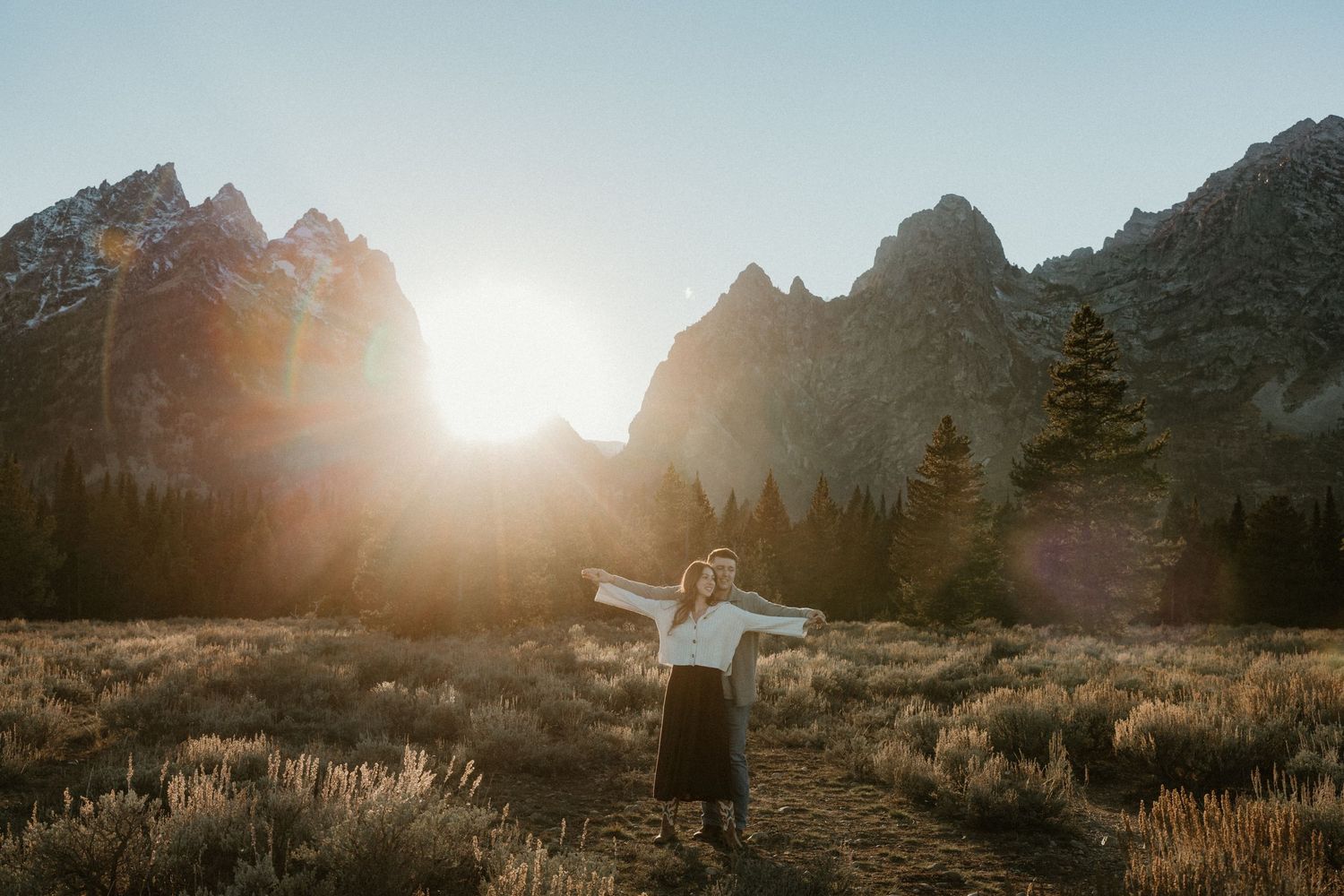 Golden sunlight illuminates a mountainous landscape as figures stand in silhouette.