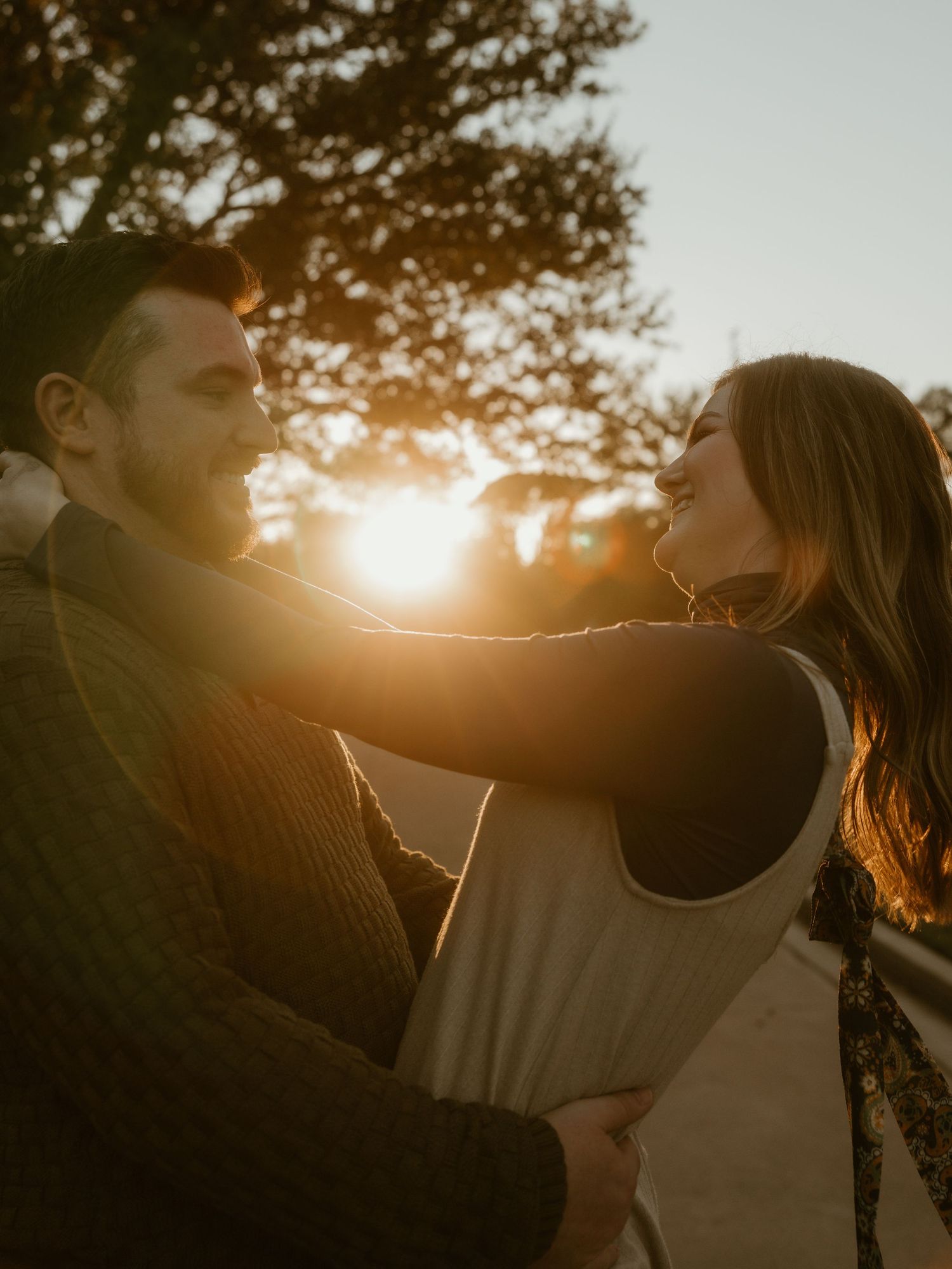 Couple embracing in golden sunset light with trees silhouetted in background.