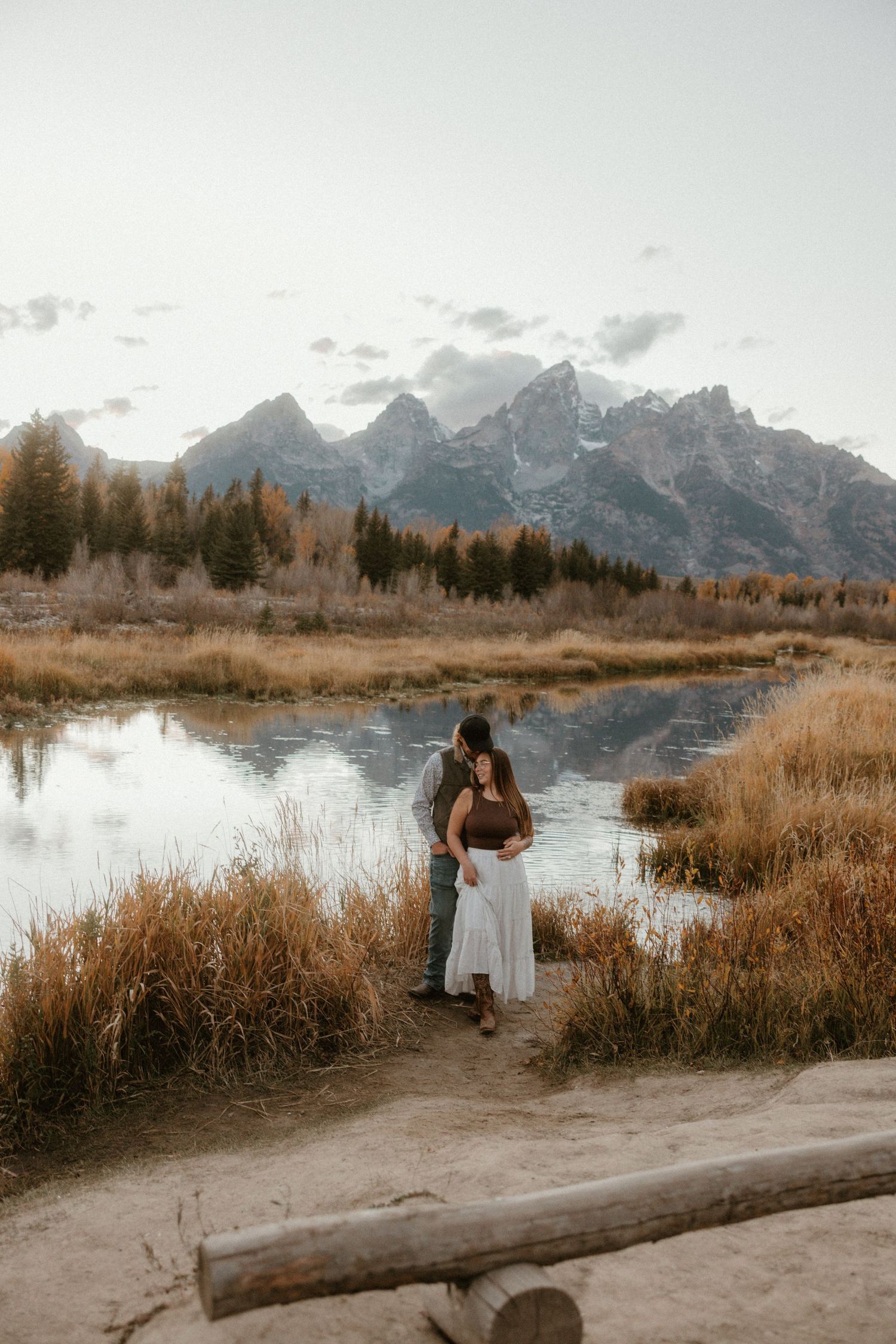 A romantic photoshoot by a lake with snow-capped mountains and autumn foliage in the background.