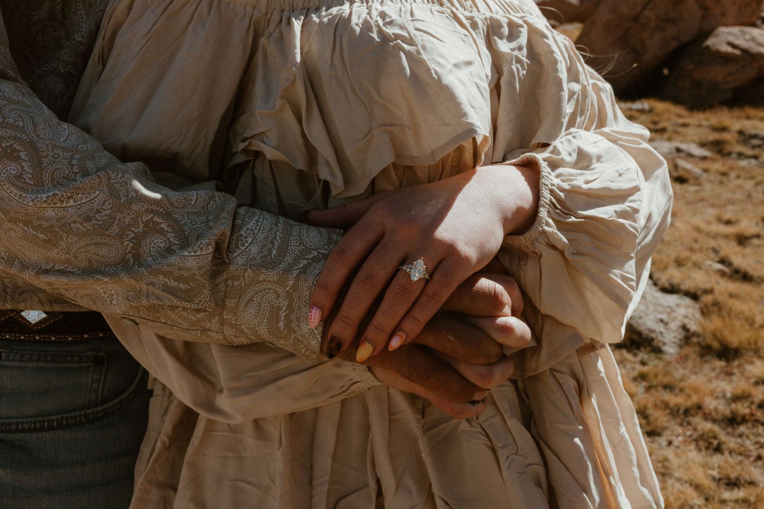 Close-up of hands clasped together against light colored fabric in natural outdoor setting.
