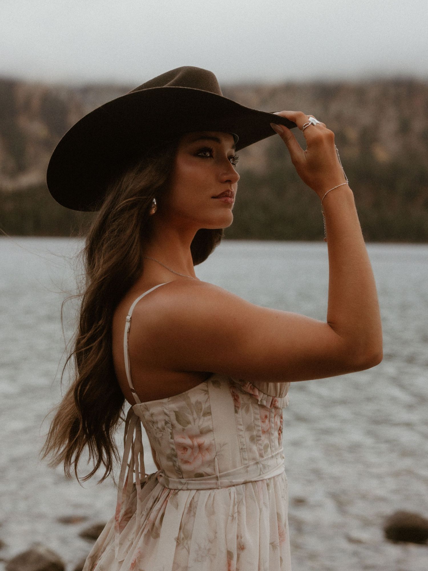 A woman in a flowy white dress poses near a lake at sunset in a series of artistic outdoor portraits.