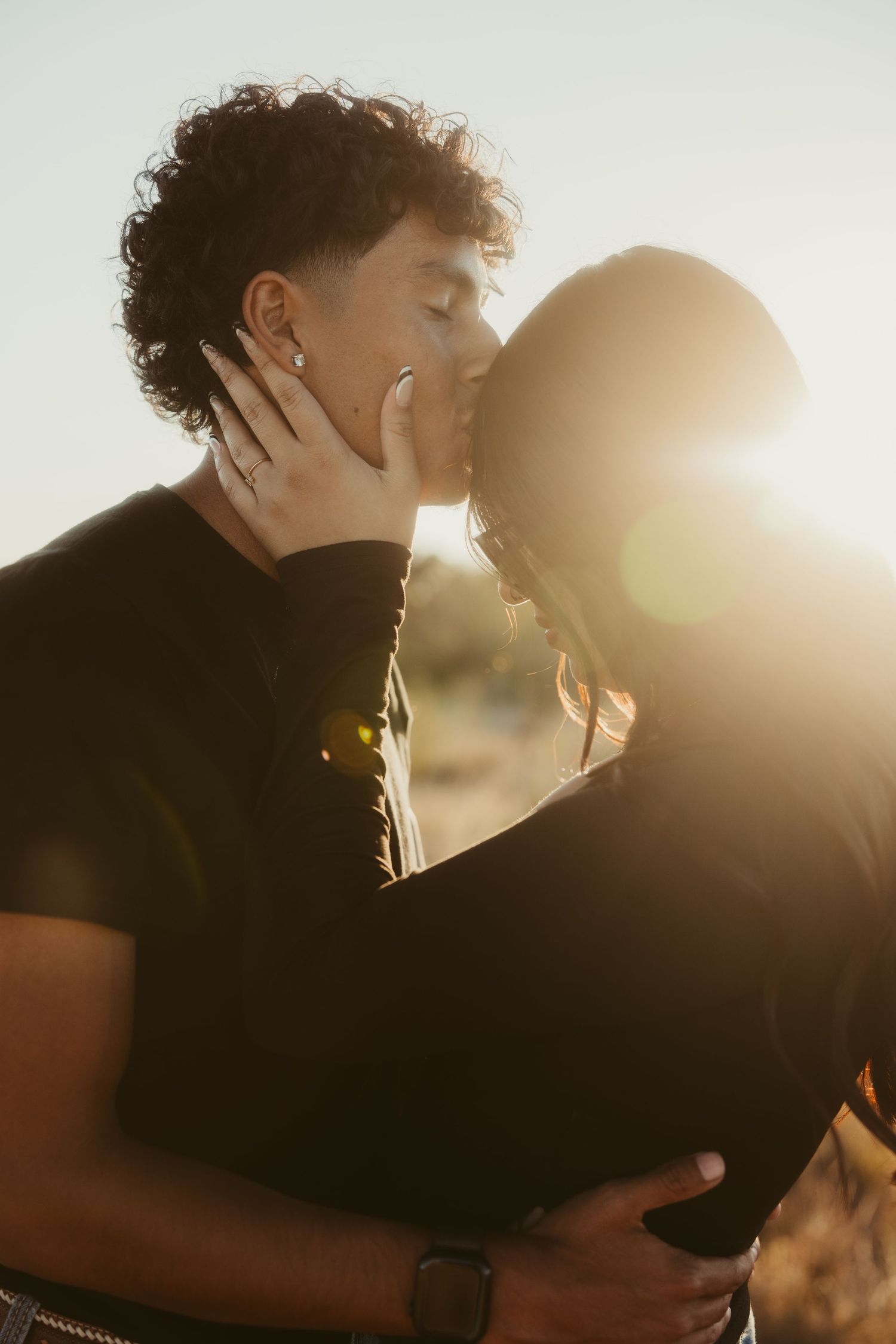 Silhouetted couple sharing intimate kiss during golden hour with sun flare.