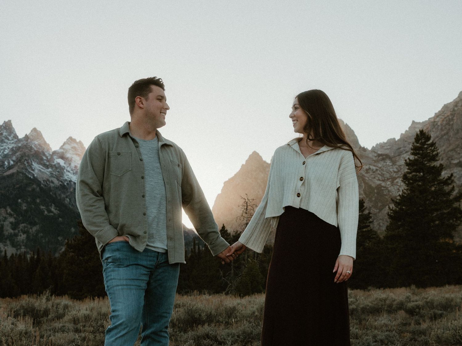 A couple shares a romantic moment against a mountainous backdrop in soft lighting.