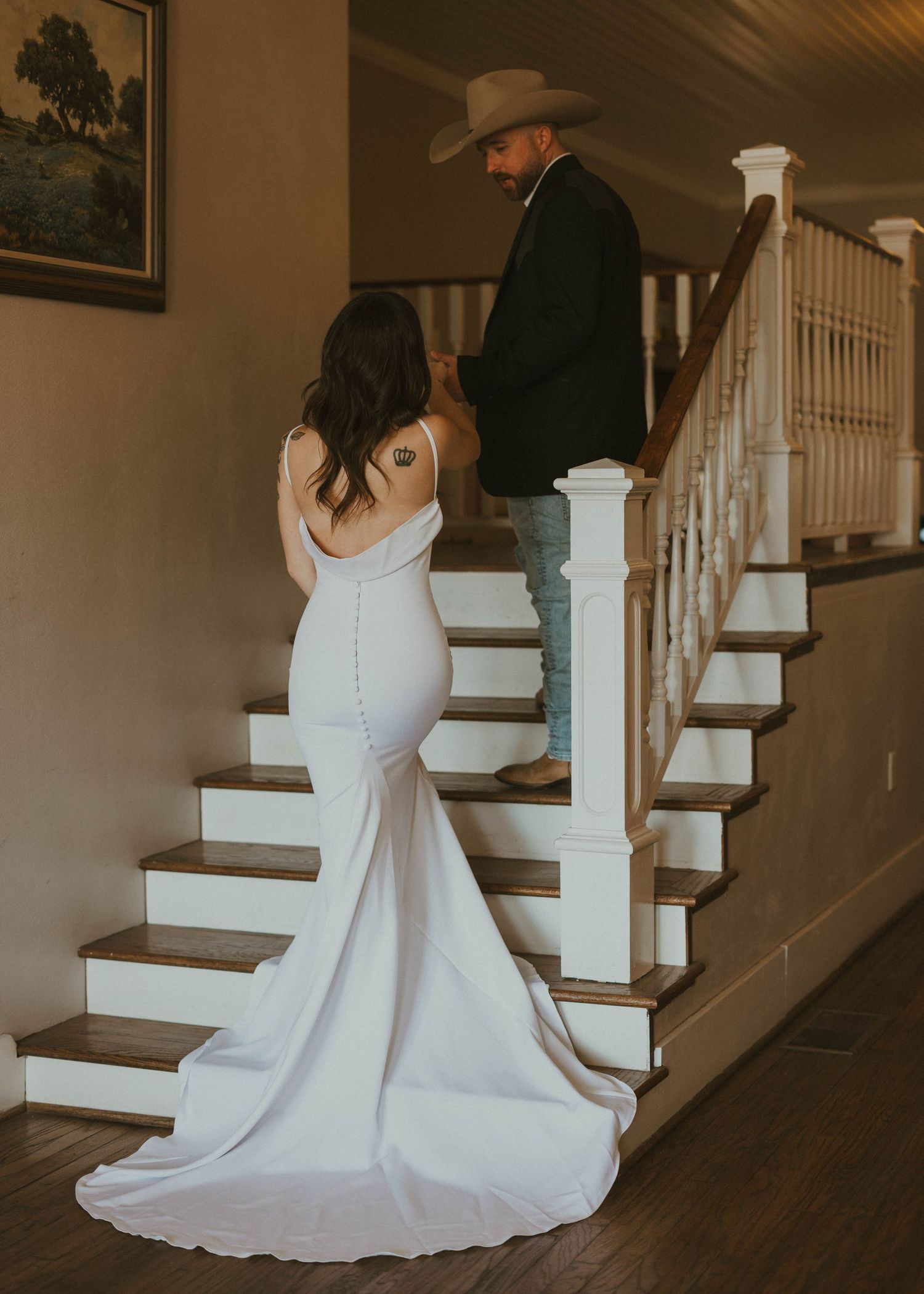 Elegant white wedding dress with flowing train photographed on wooden staircase with white railings.