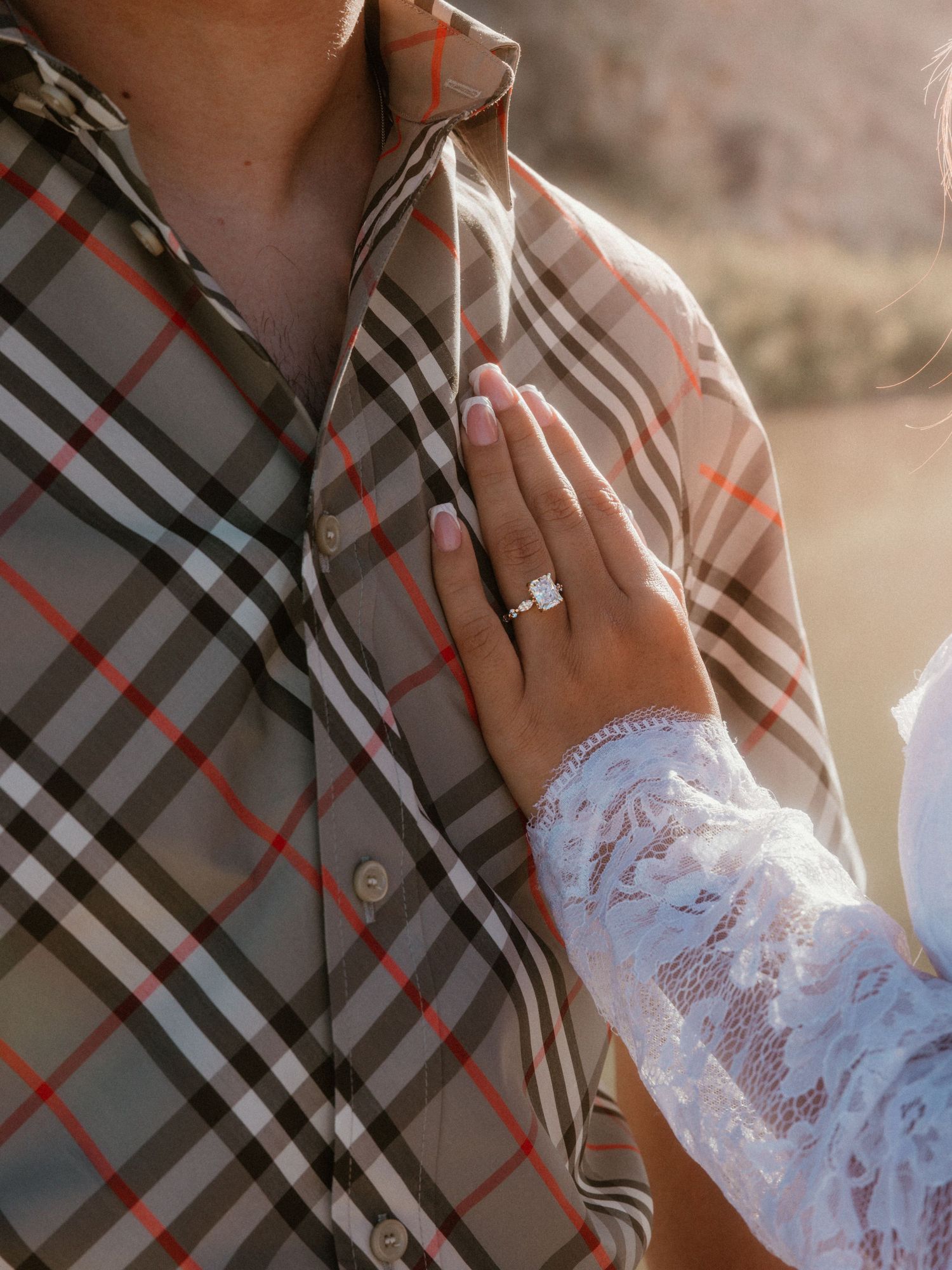 Close-up of plaid shirt and lace sleeve with engagement ring visible.