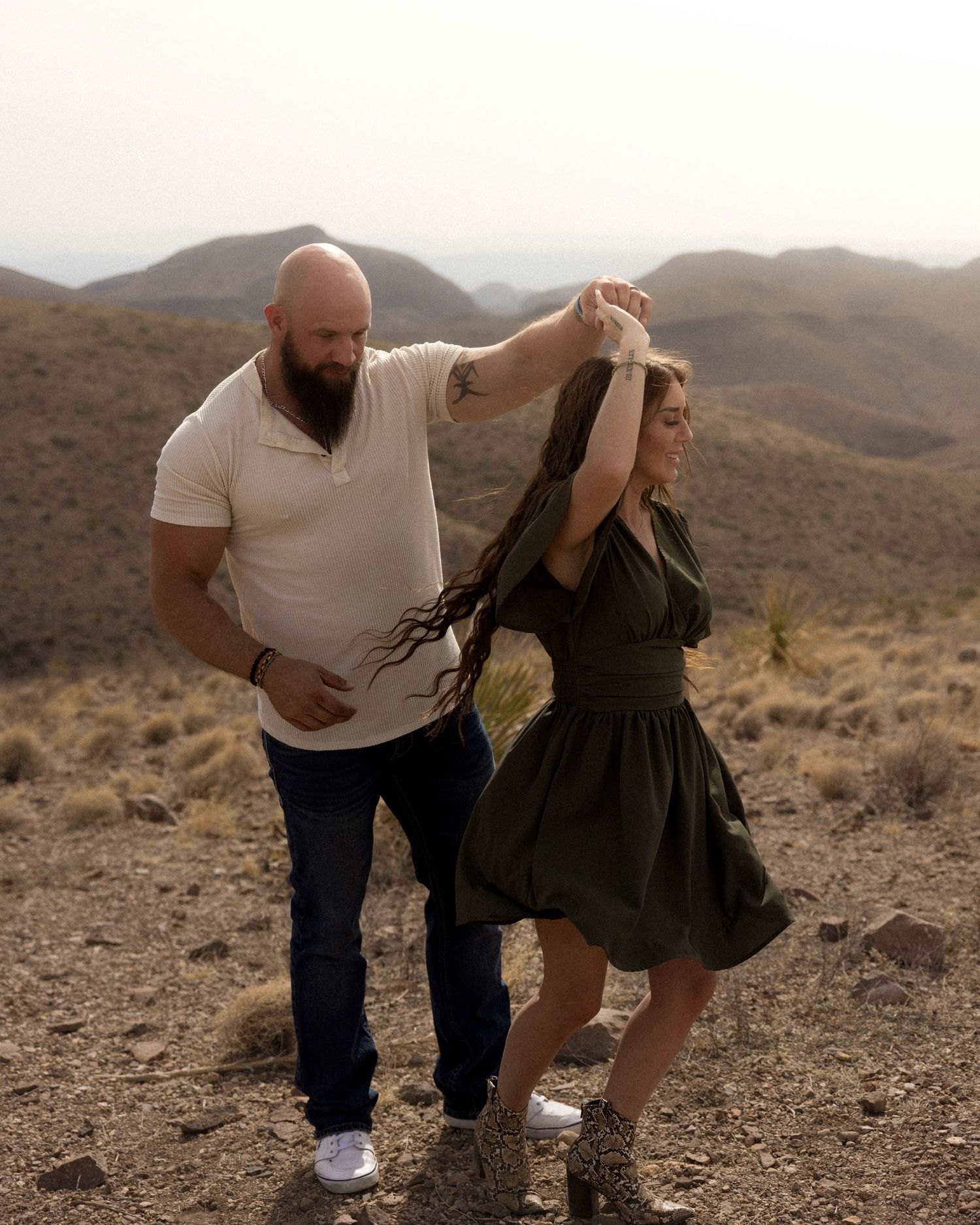 Dancing couple shares a playful moment in the desert with mountains behind them.