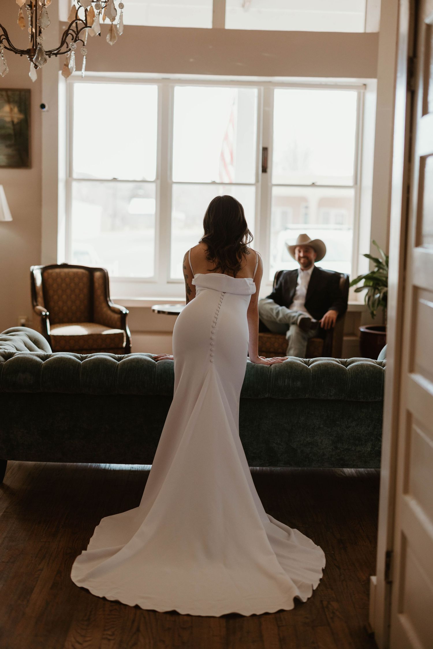 Wedding dress displayed in living room setting with dark couch and large windows.