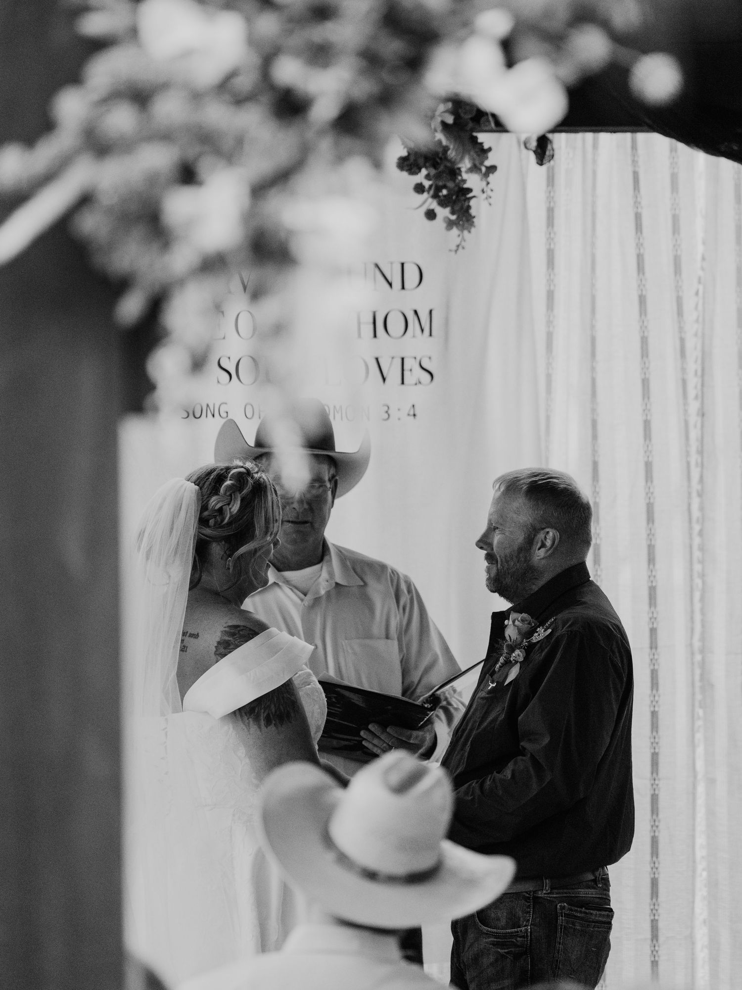 Black and white wedding ceremony photo with text overlay and draped backdrop.