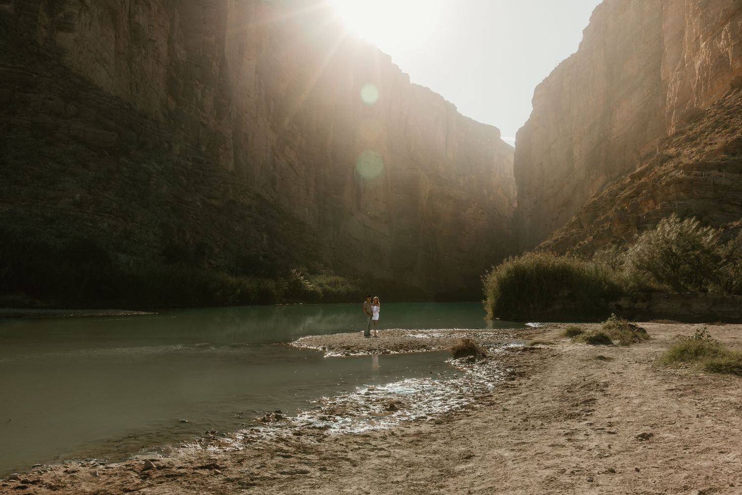 A scenic canyon landscape with river and figures in the distance on a rocky shore.
