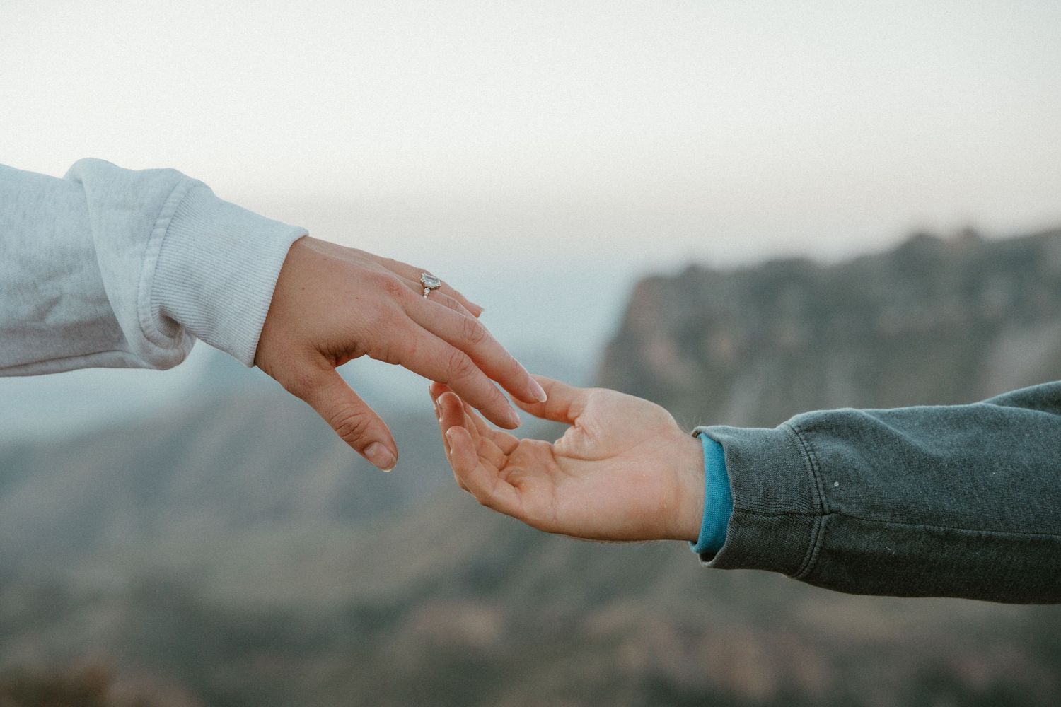 Hands reaching towards each other against a mountainous landscape backdrop.