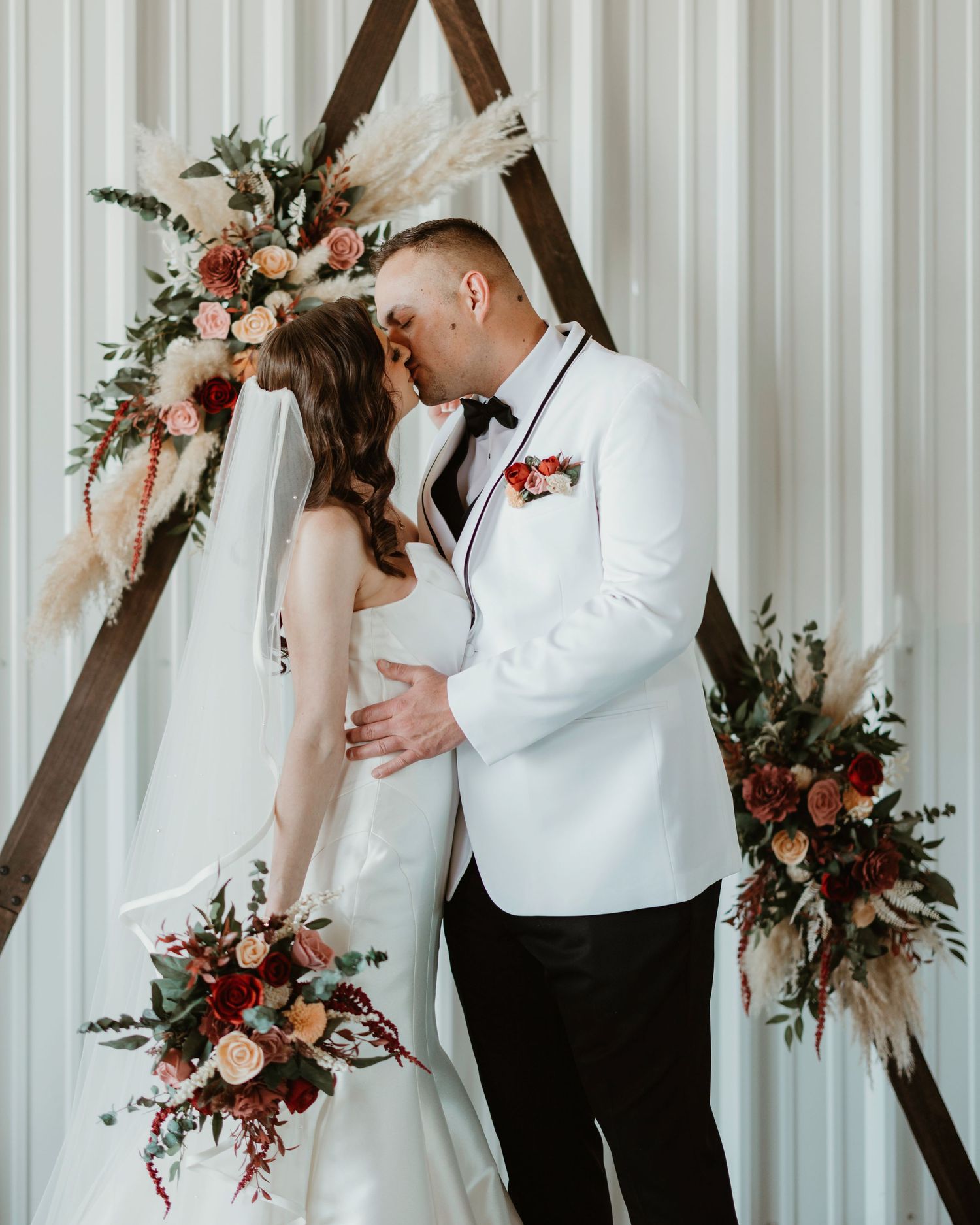 Indoor wedding portraits with wooden triangle arch and pink floral decorations.