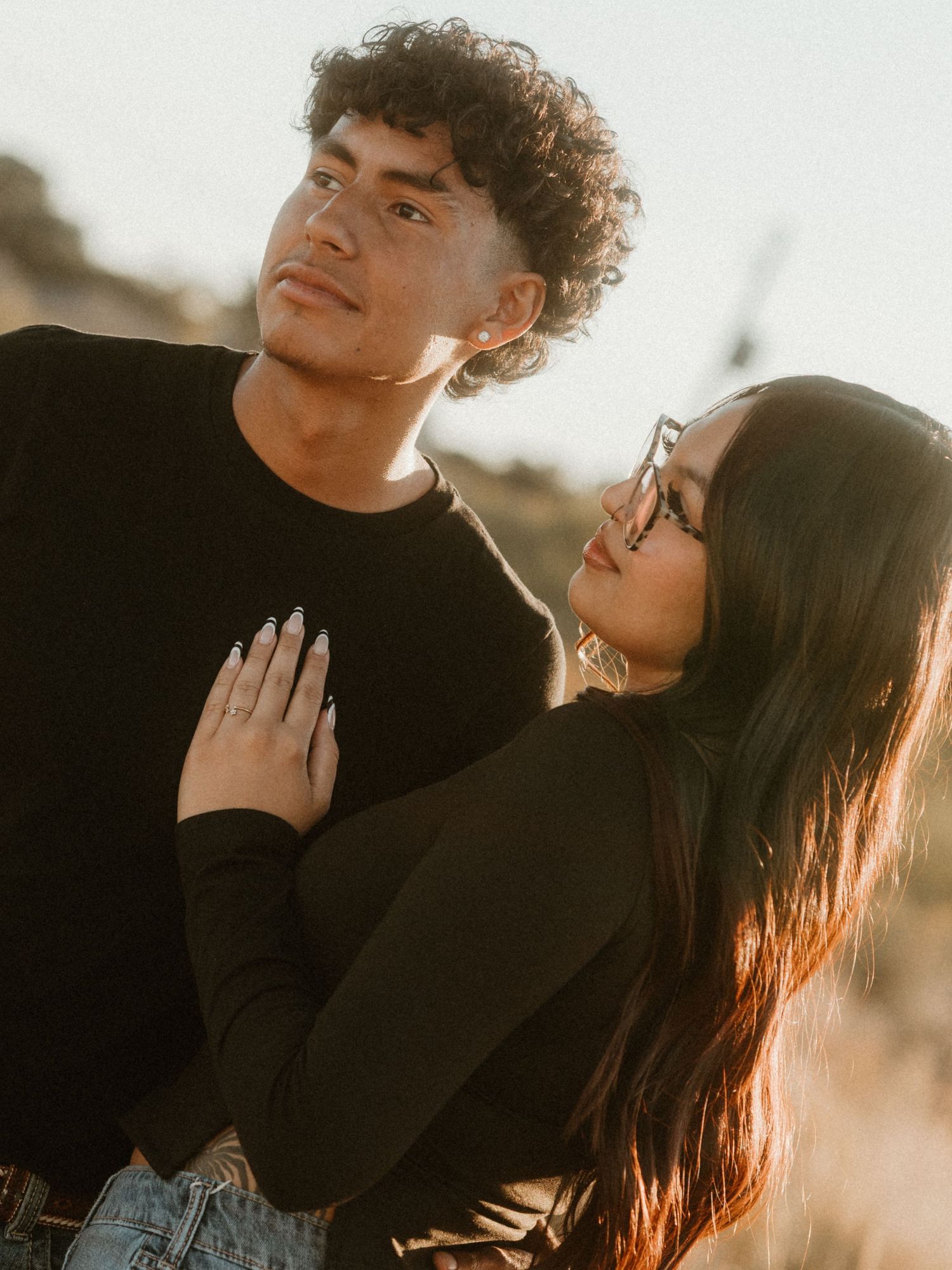 Intimate portrait of couple in black sweaters against sunset backdrop.
