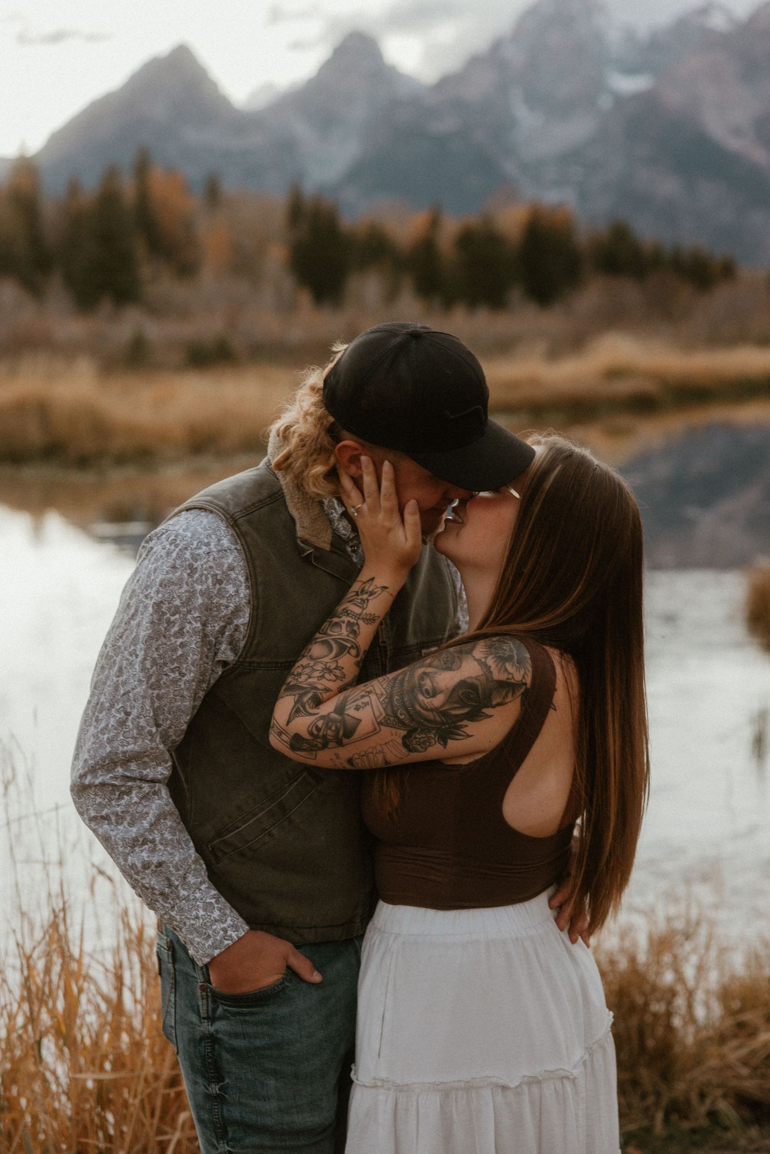 Intimate couple embracing by a scenic mountain lake during golden hour with fall colors.