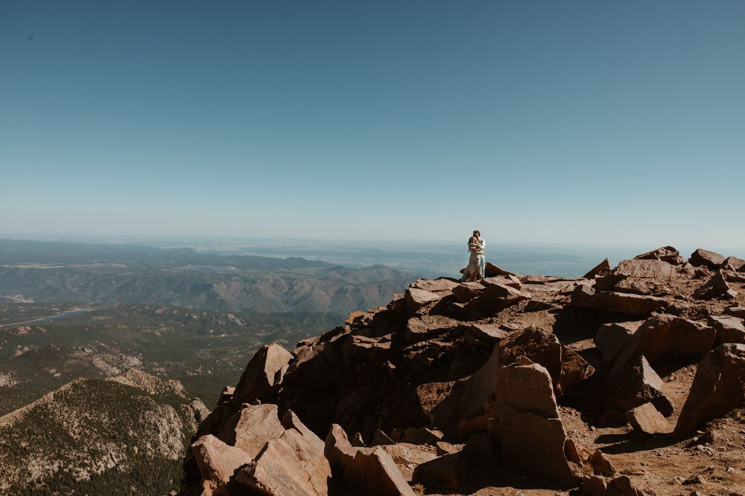 Lone silhouette stands atop rocky mountain summit with panoramic views of distant peaks.