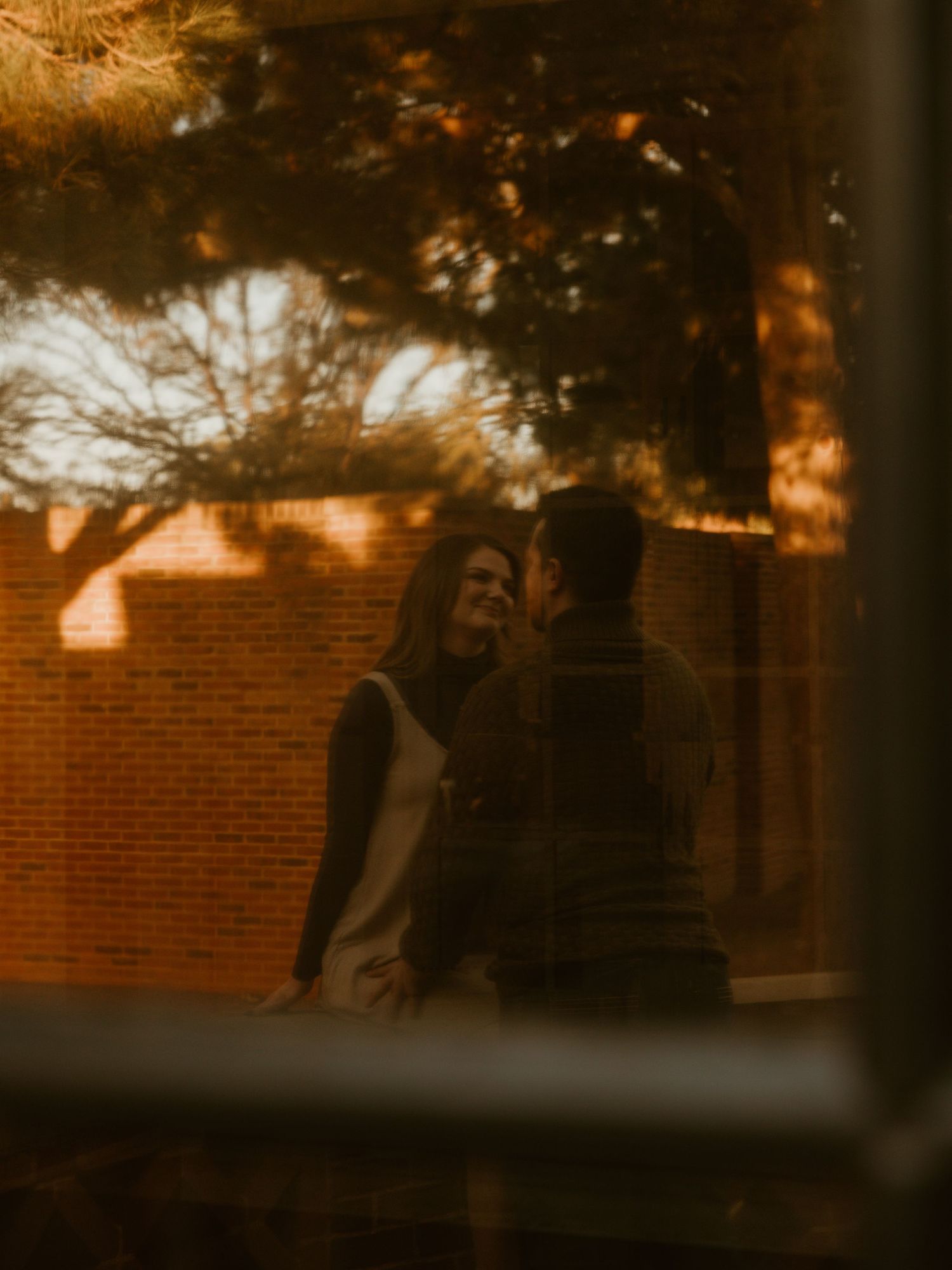 Silhouetted couple embracing during golden hour with brick building in background.