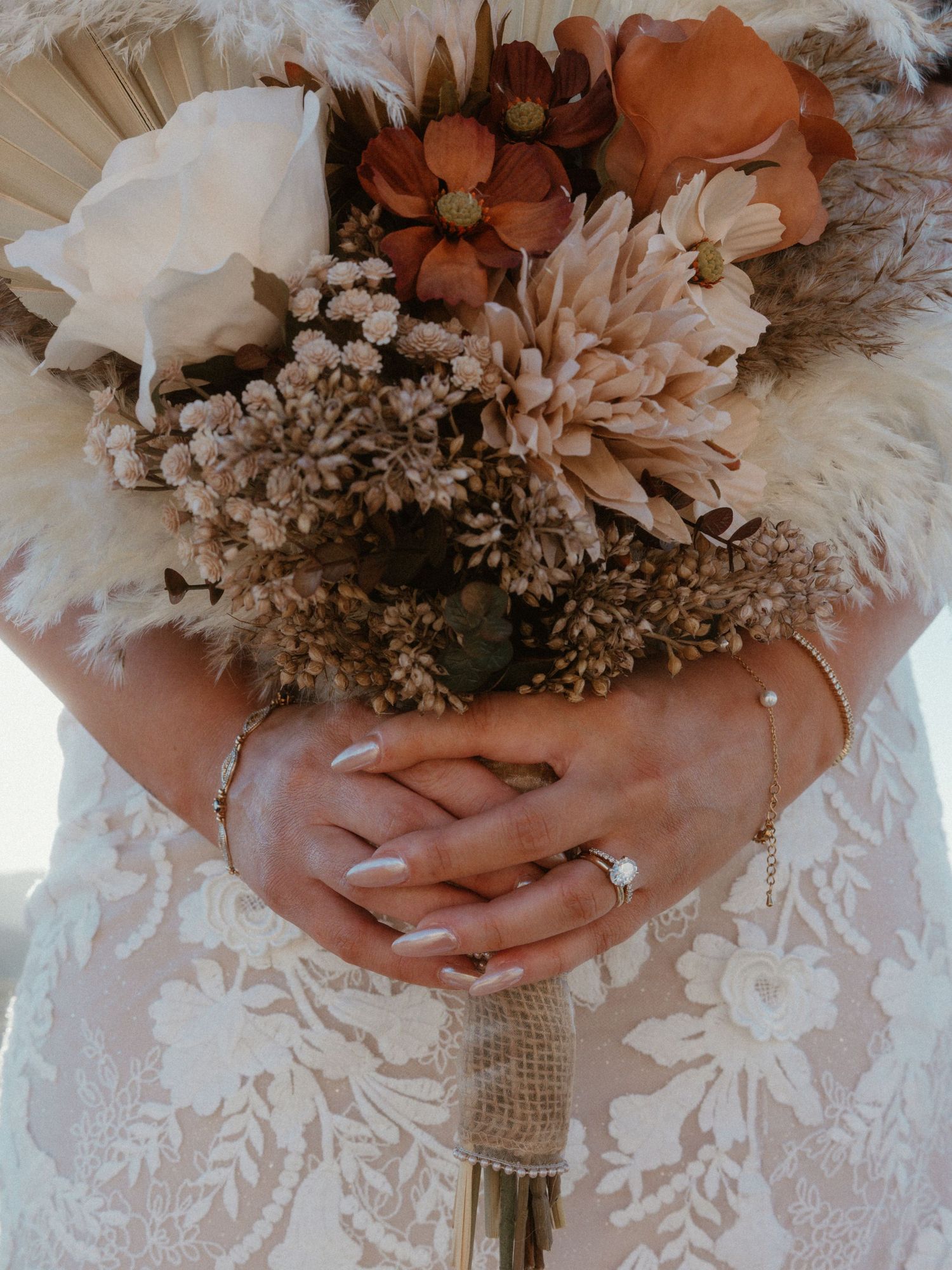 Close-up of a bridal bouquet with white and terracotta flowers wrapped in burlap.