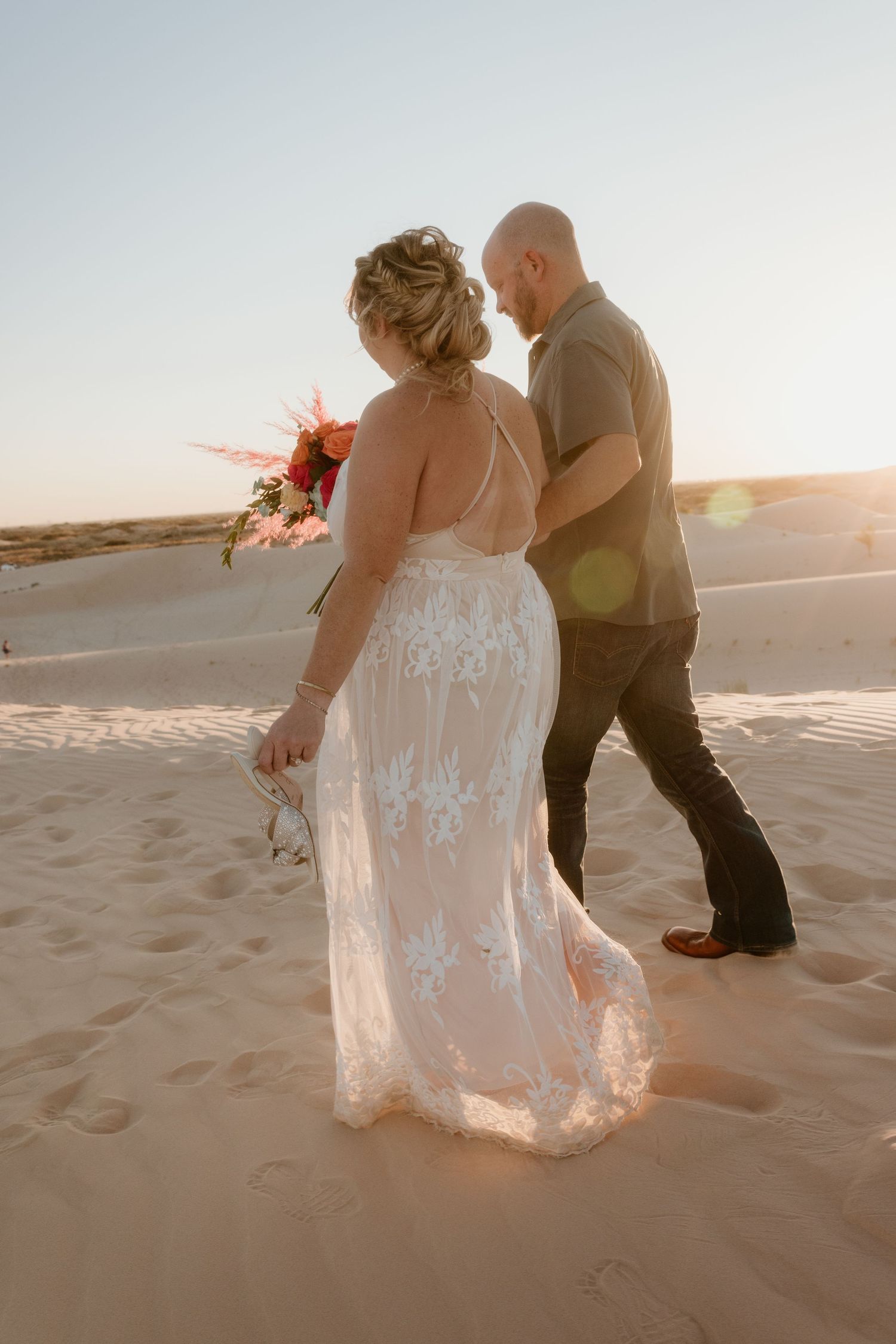A romantic moment captured on sandy dunes during a desert wedding photoshoot.
