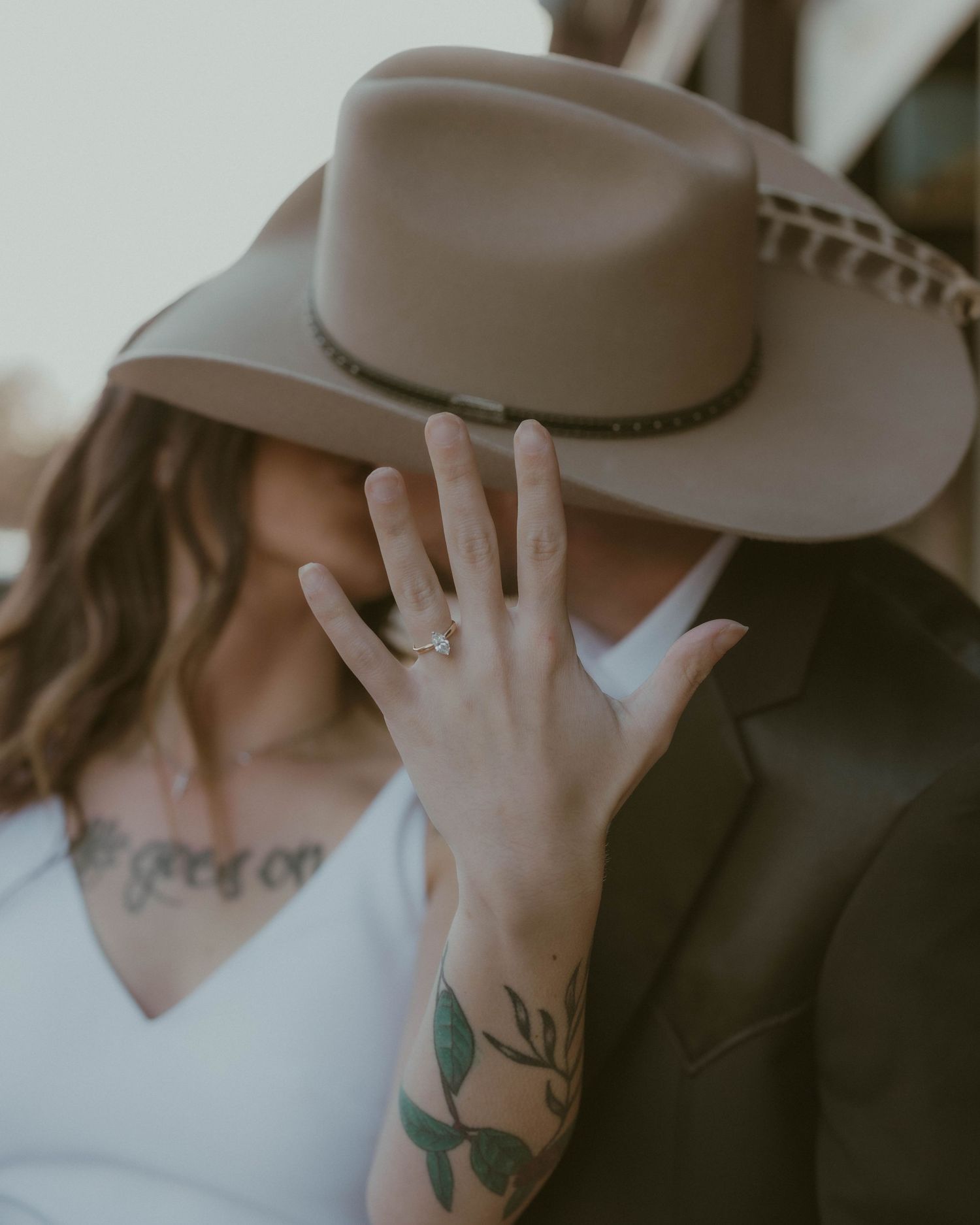 Close-up shots of hands adjusting a gray cowboy hat with visible tattoos.