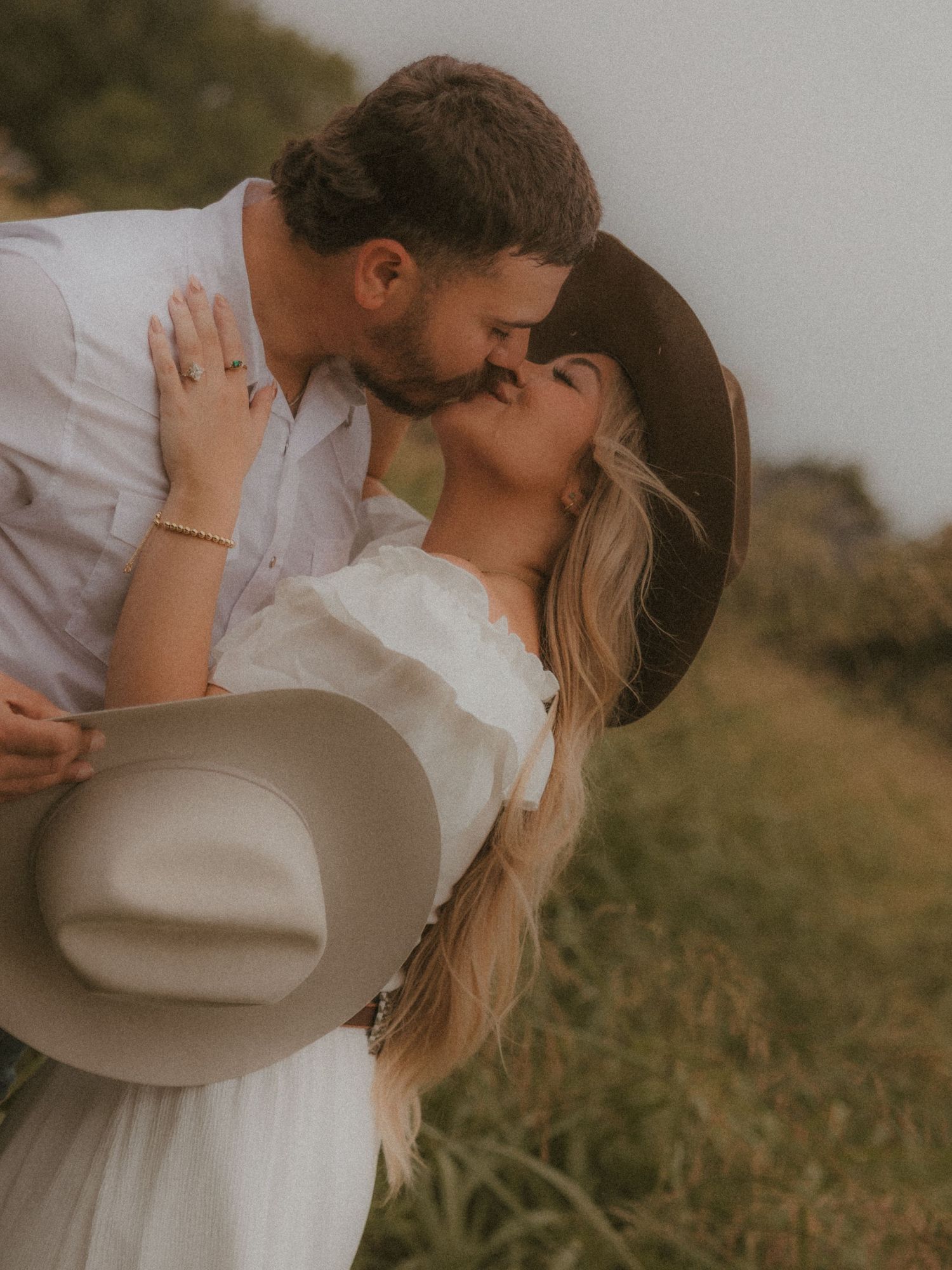 Romantic couple in western attire sharing intimate moments in a field.