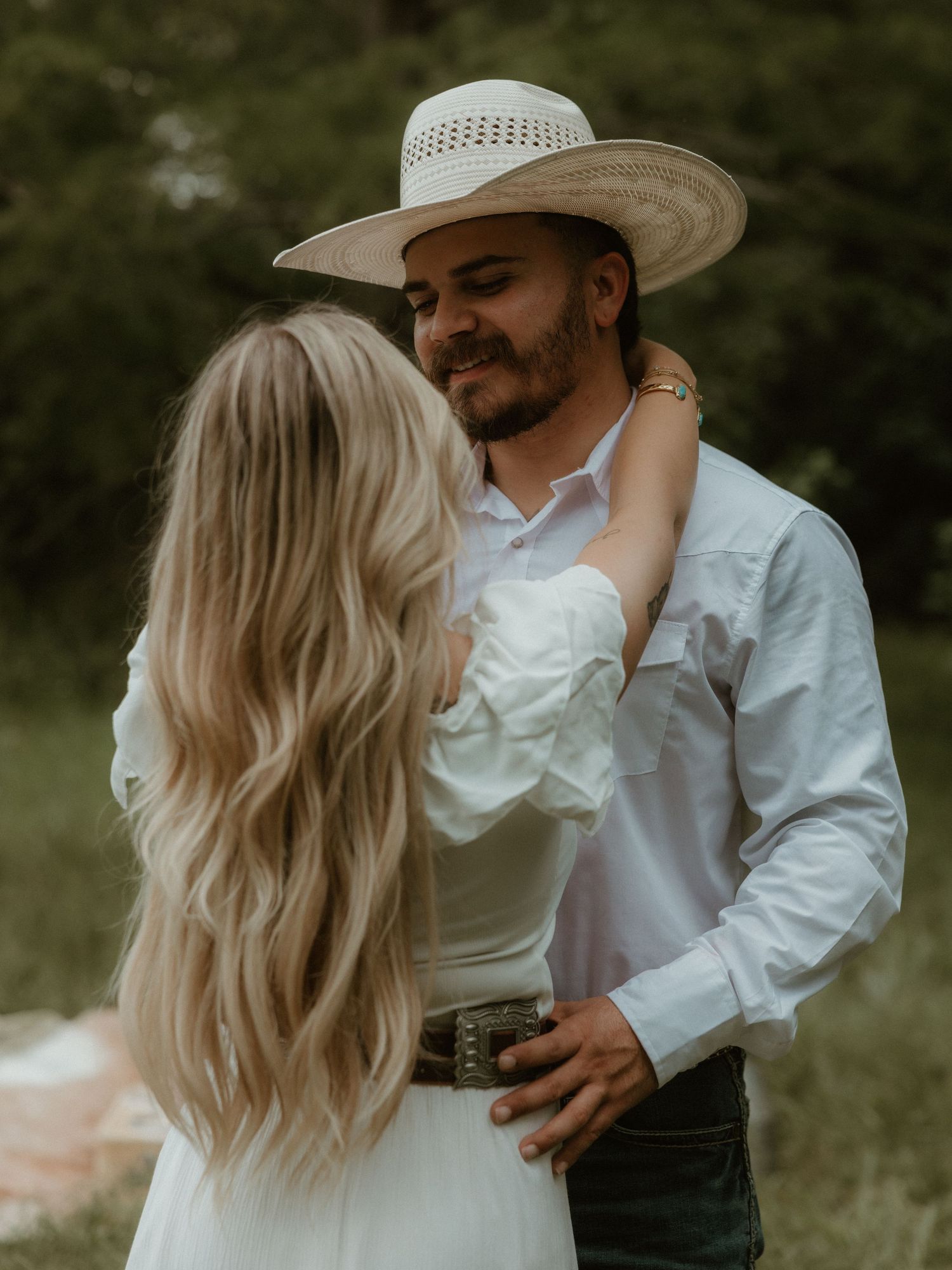 A couple in country western clothing embracing in a romantic outdoor photoshoot.