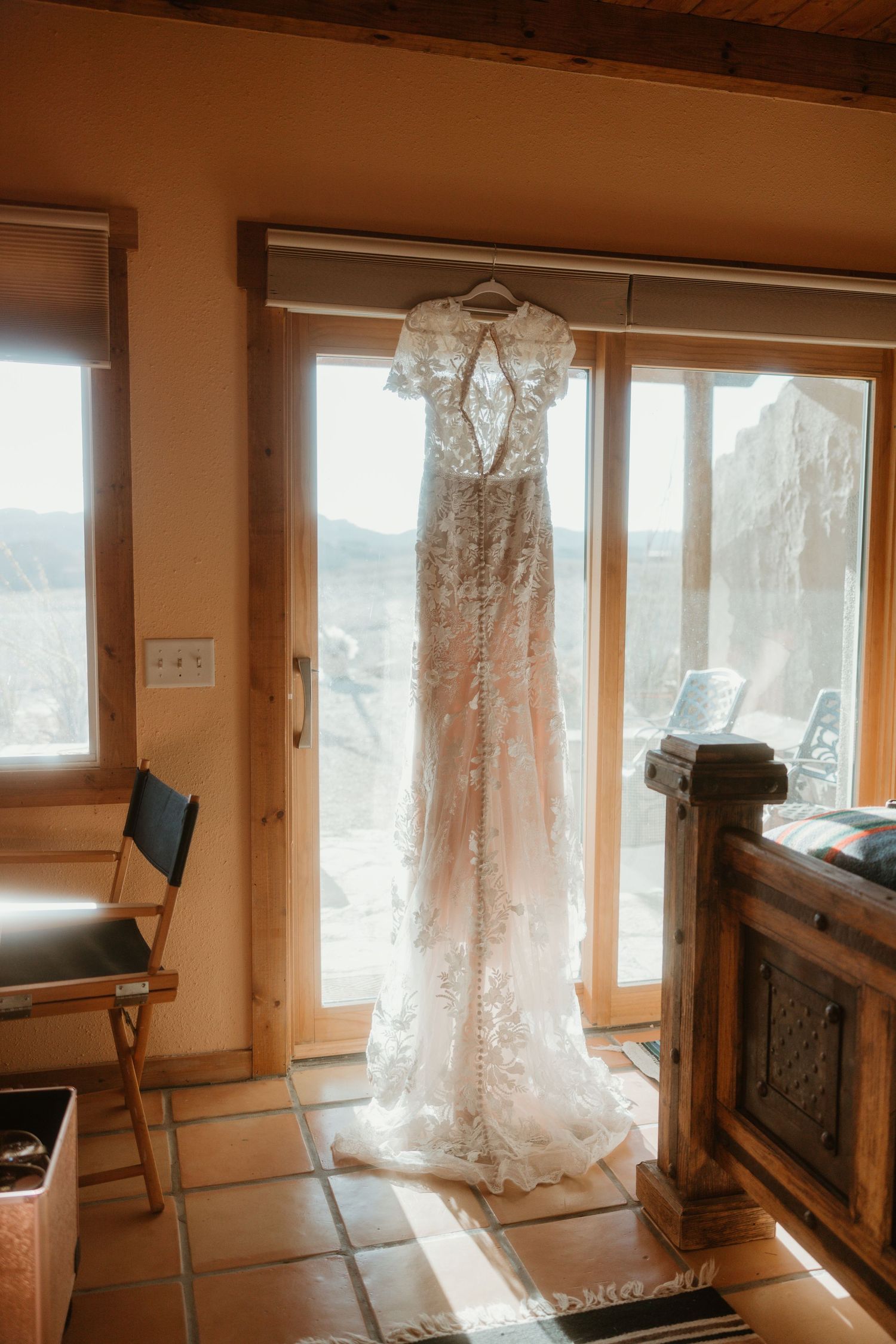 A sunlit room with large windows displaying a hanging lace wedding dress.