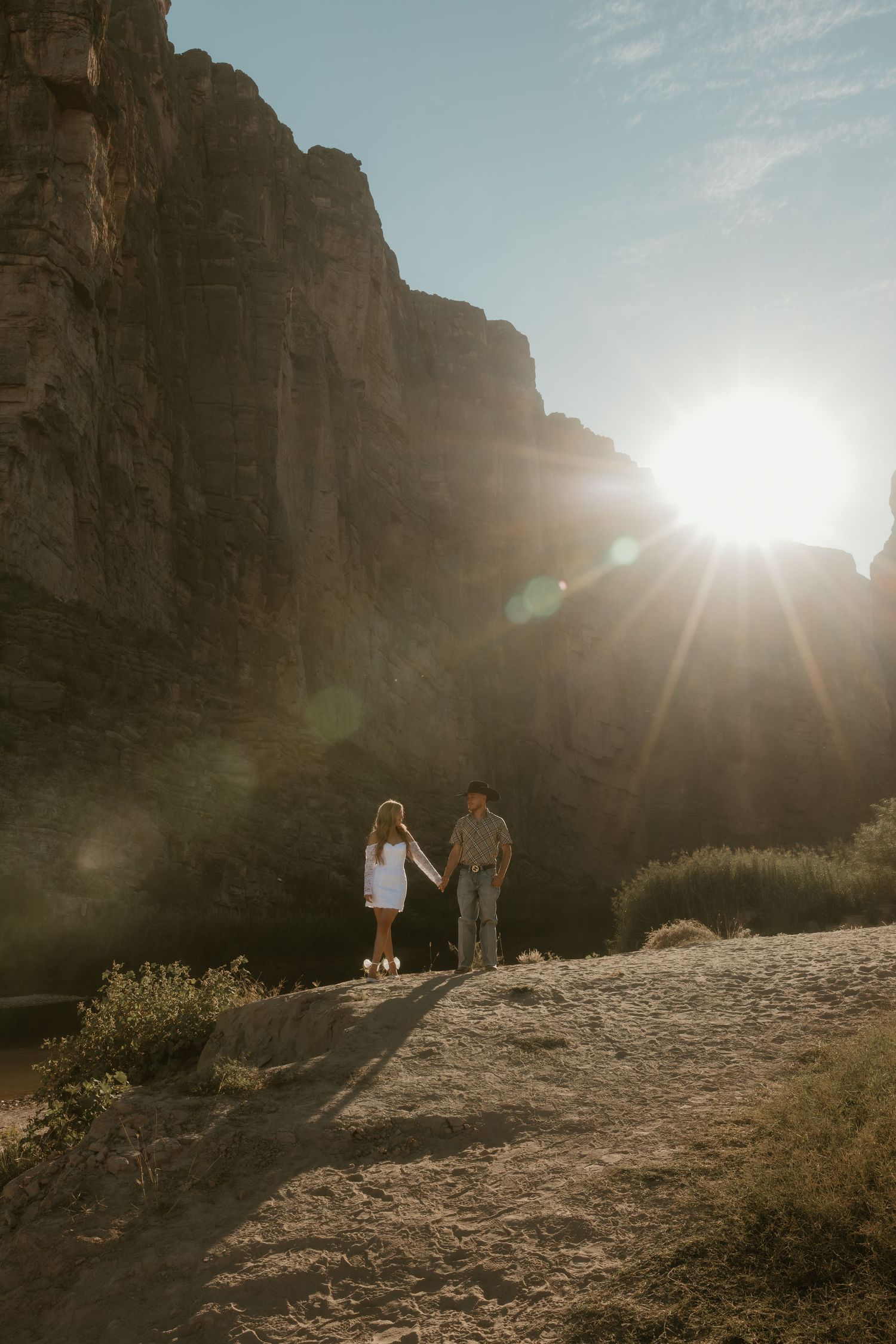 Silhouettes of a couple standing on a hill against dramatic mountain cliffs at sunset.