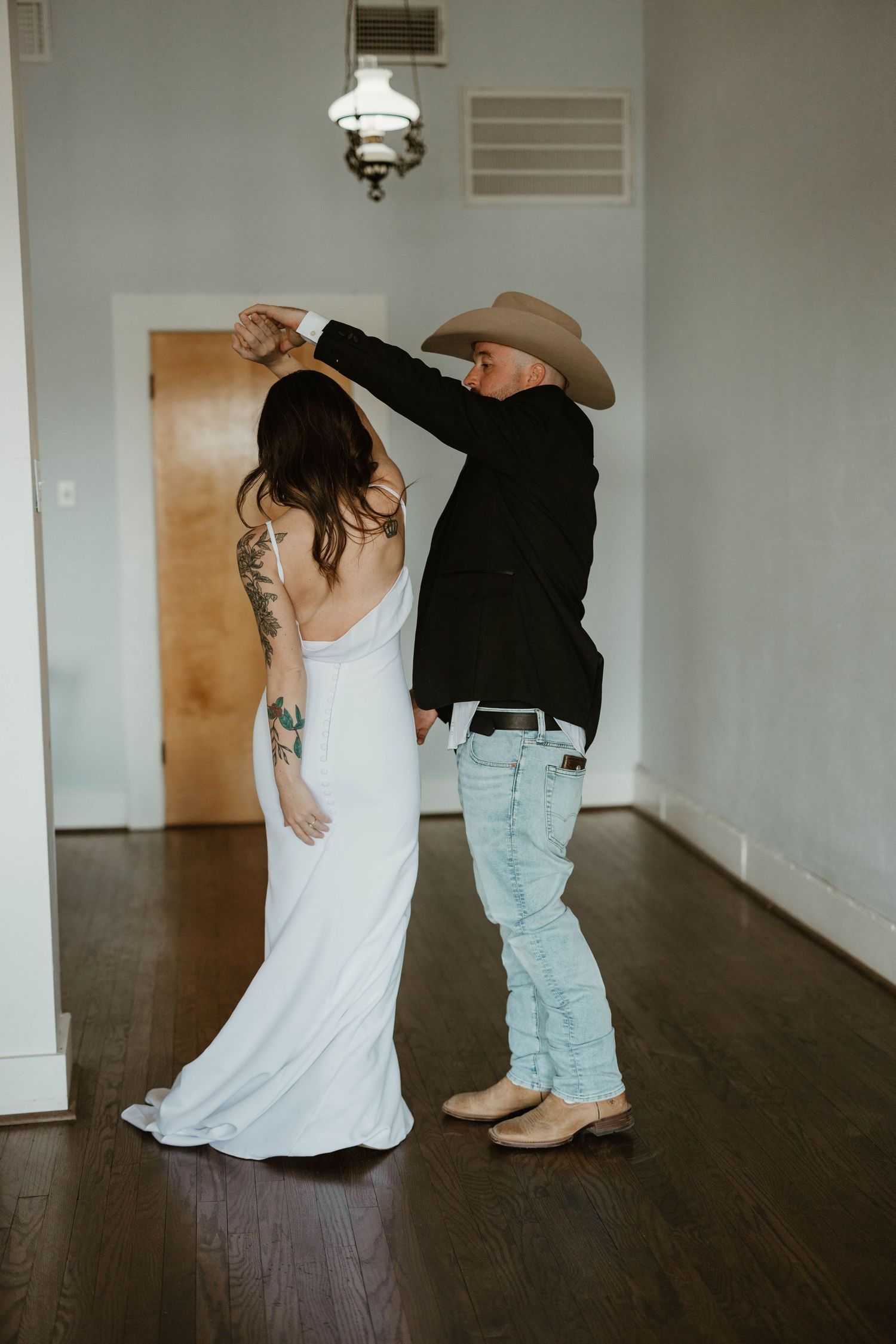 Wedding couple dancing on dark hardwood floor in rustic indoor setting.