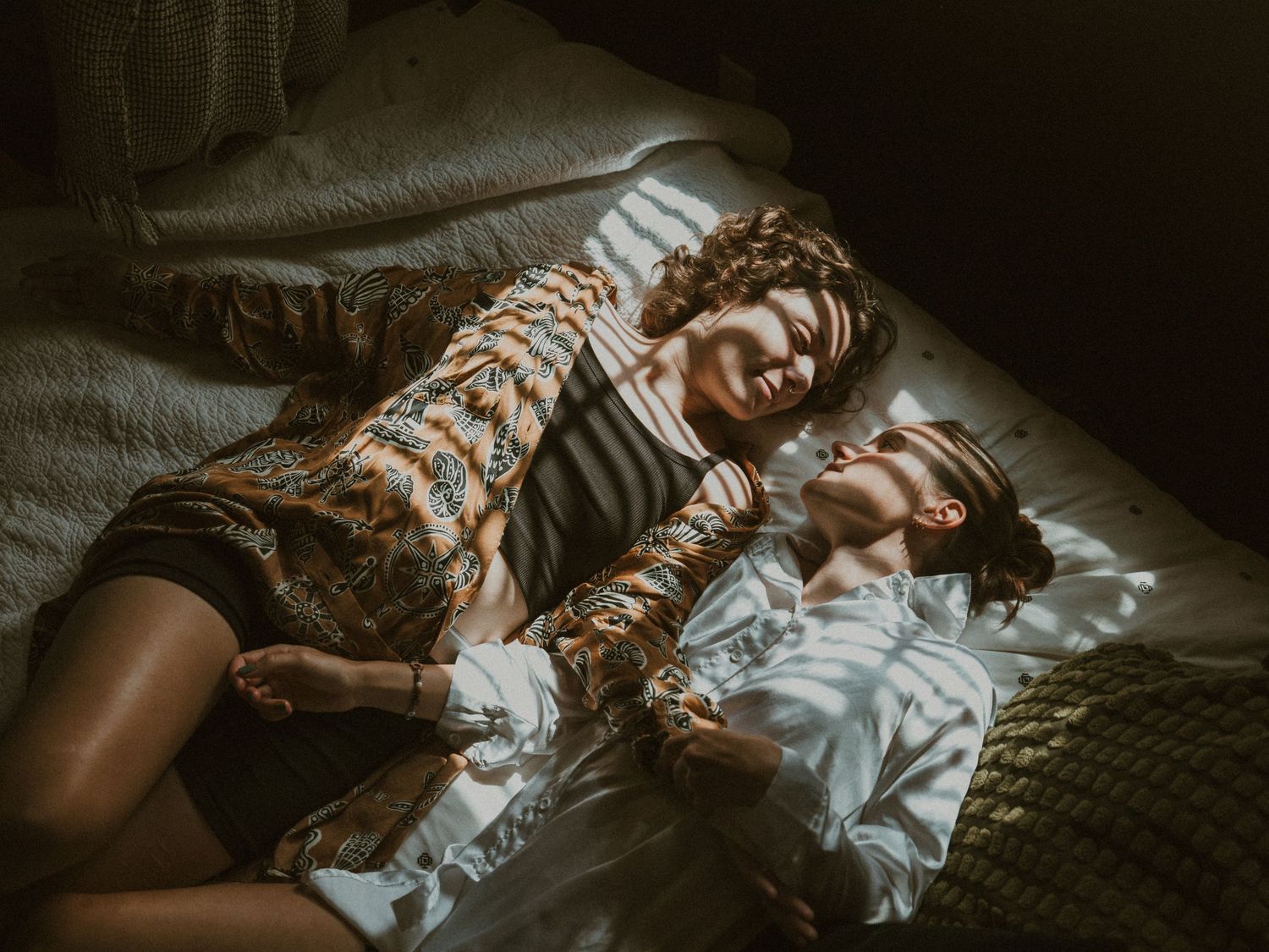 Two people lying close together on a bed in moody, dark lighting.