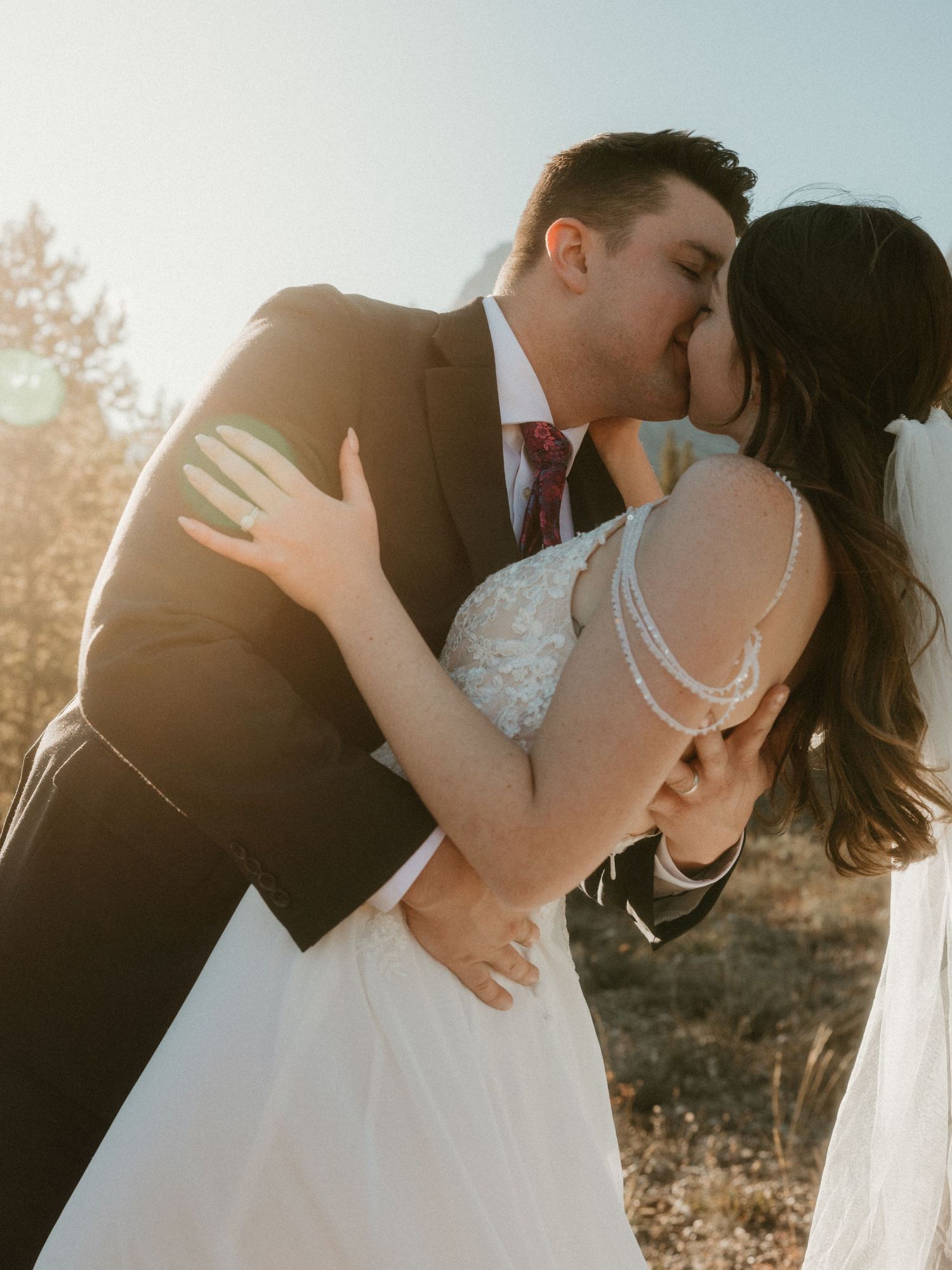 A couple shares an intimate kiss against a sunlit backdrop during their wedding ceremony.