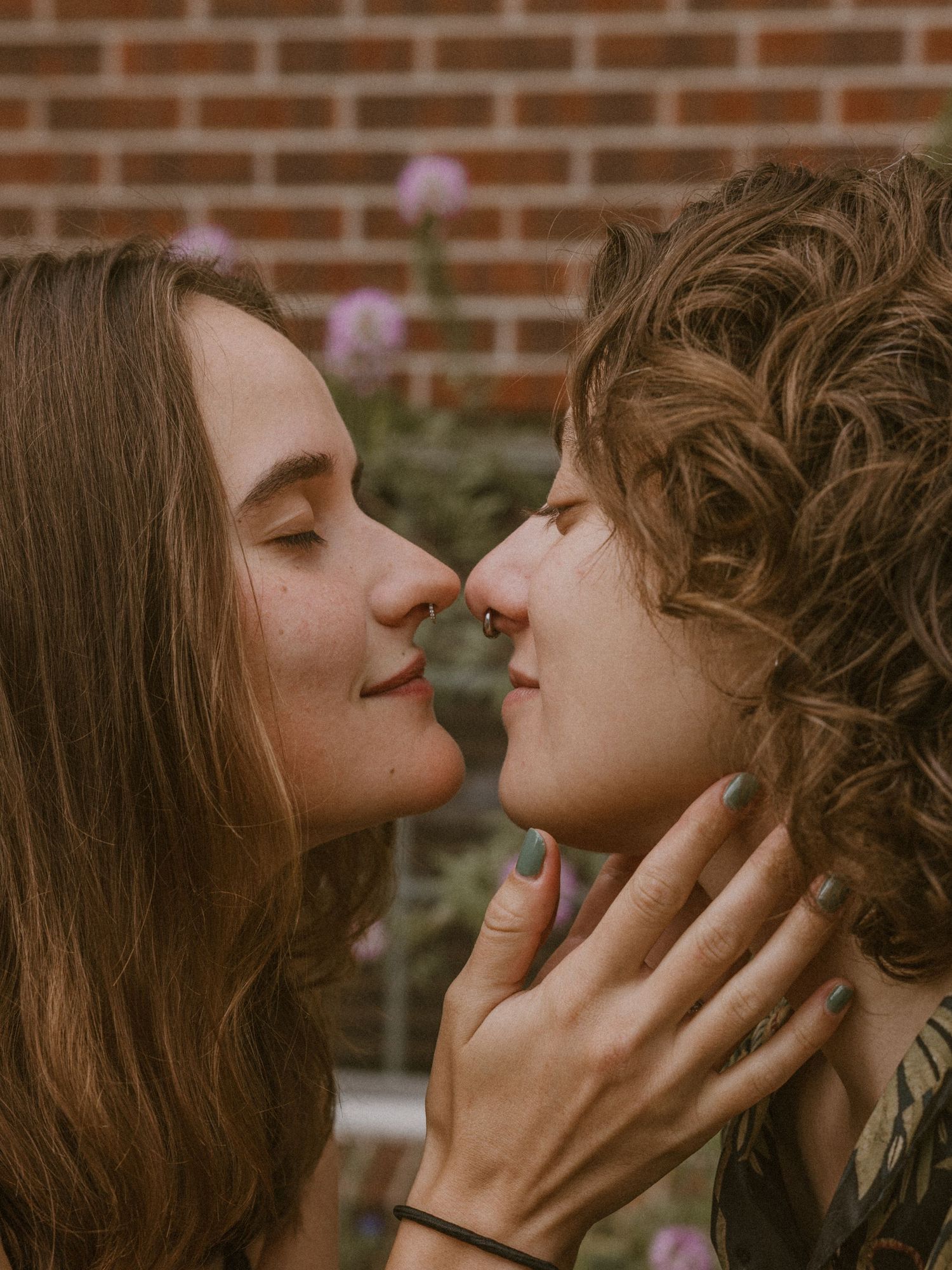 A couple sharing a tender moment against a brick wall background.
