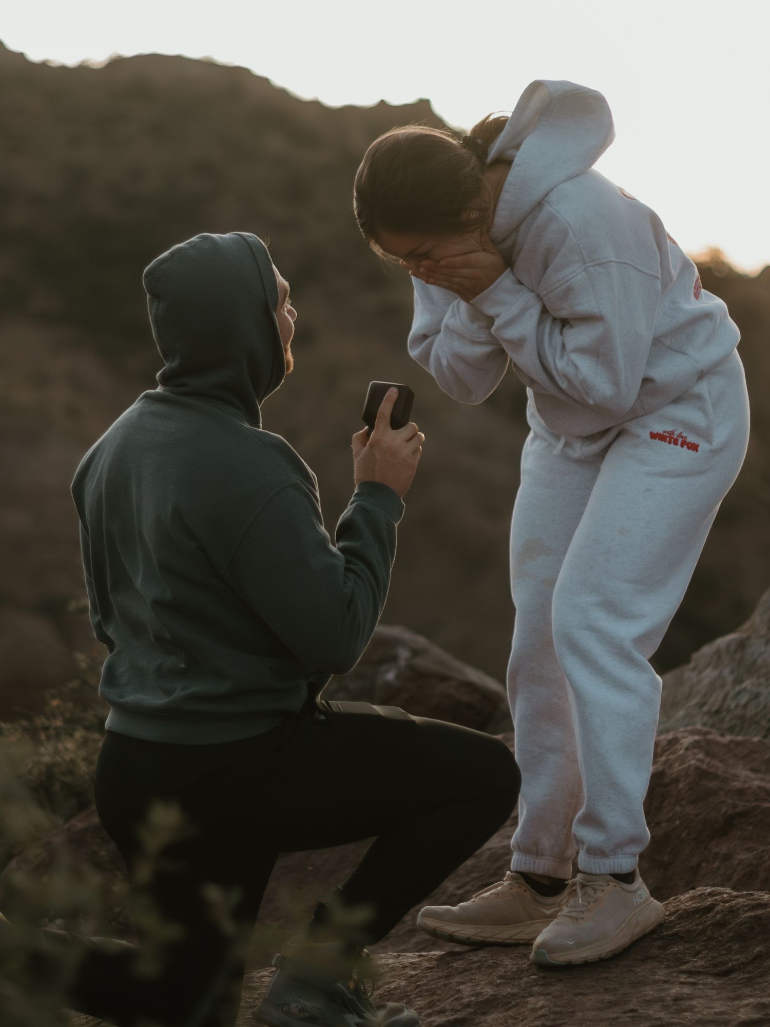 A couple sits together on rocky terrain at sunset sharing a tender moment in the mountains.