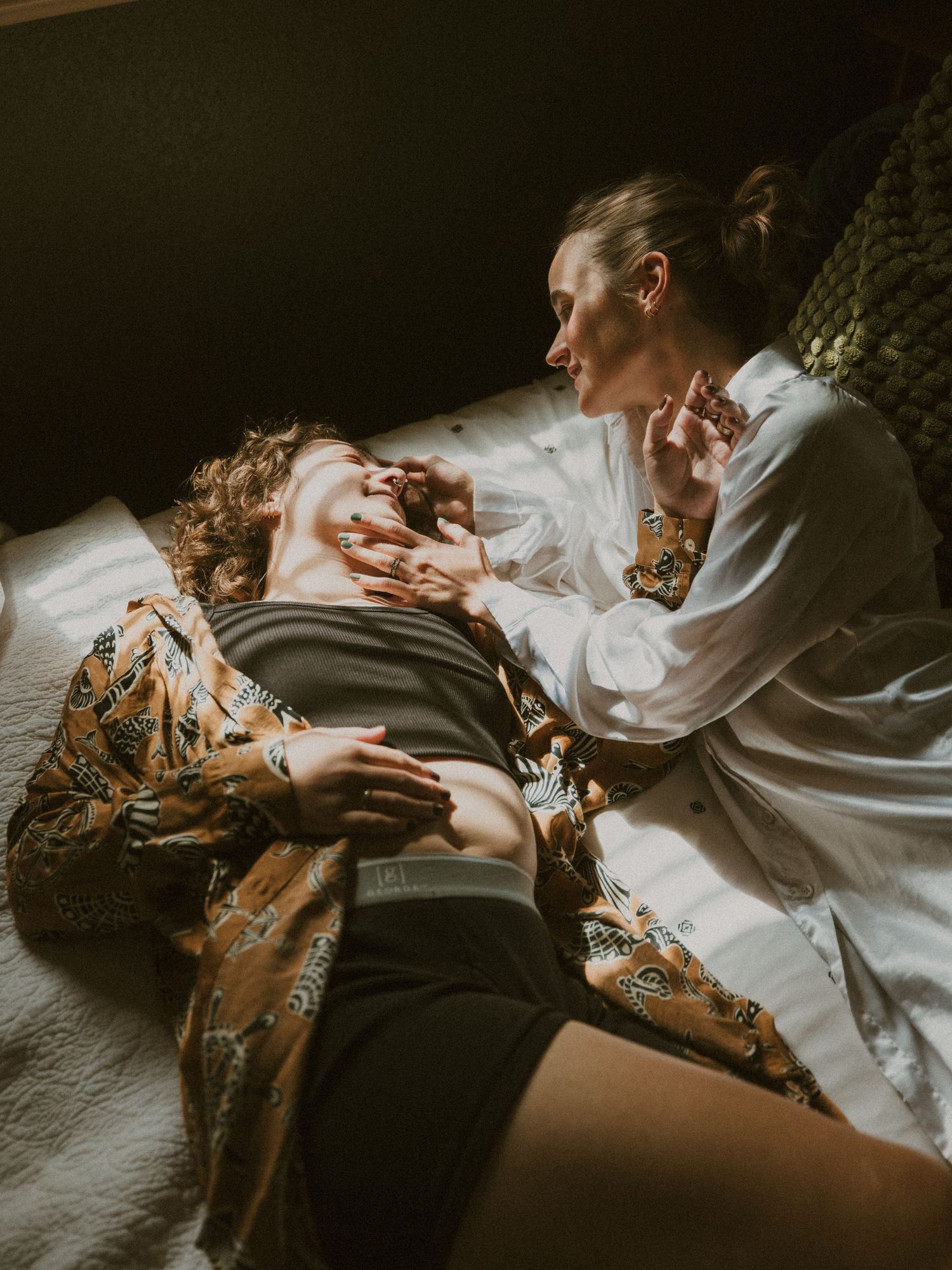 Artistic moody photograph of people relaxing together on white bedding.