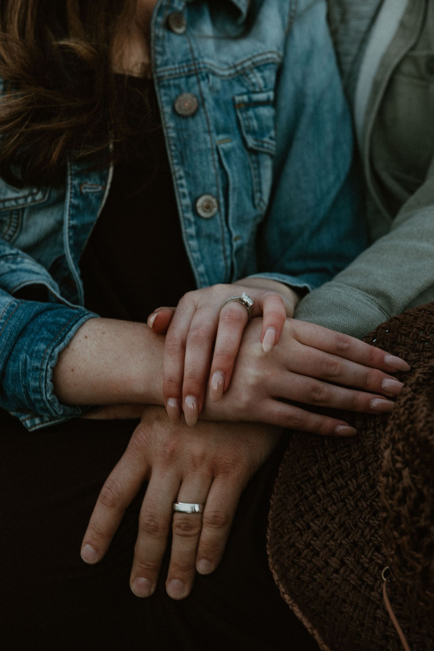Close-up of hands with wedding rings resting on brown textured surface.