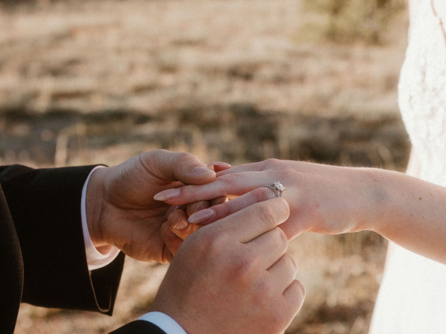 Hands exchanging wedding rings during an outdoor ceremony.
