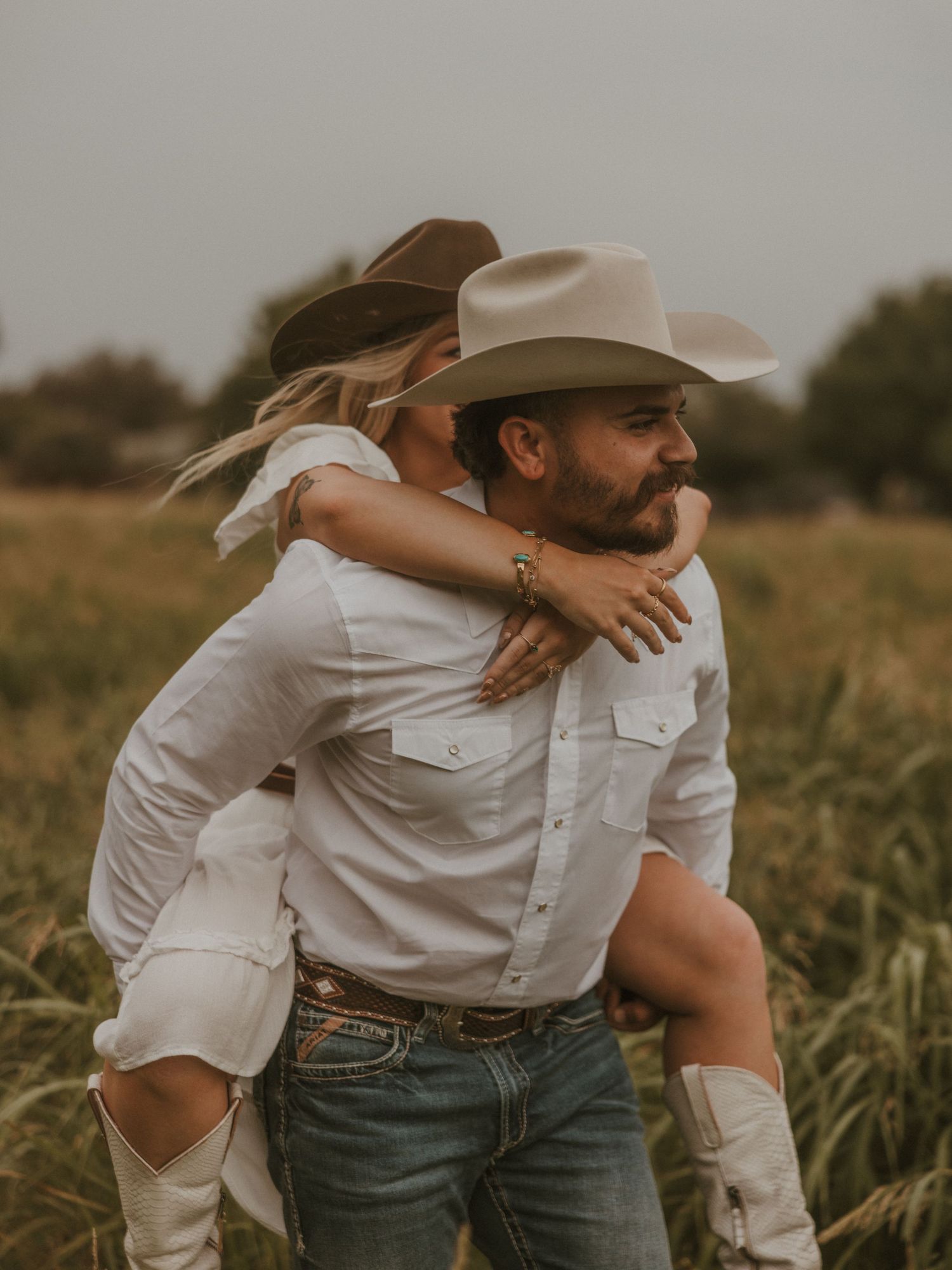 Couple in western wear sharing joyful moments in tall grass.