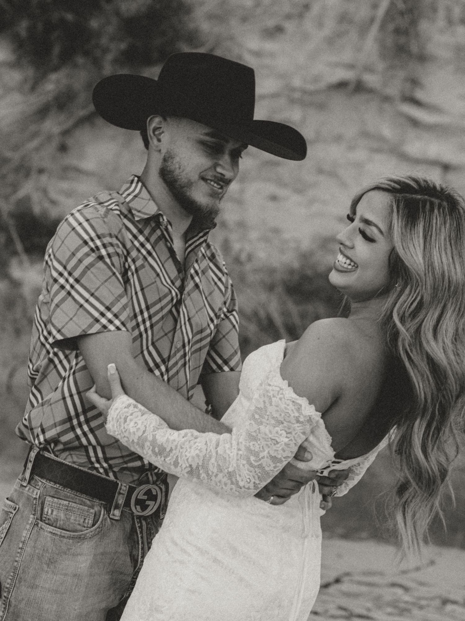 Black and white portrait of a couple in western attire sharing a joyful moment.