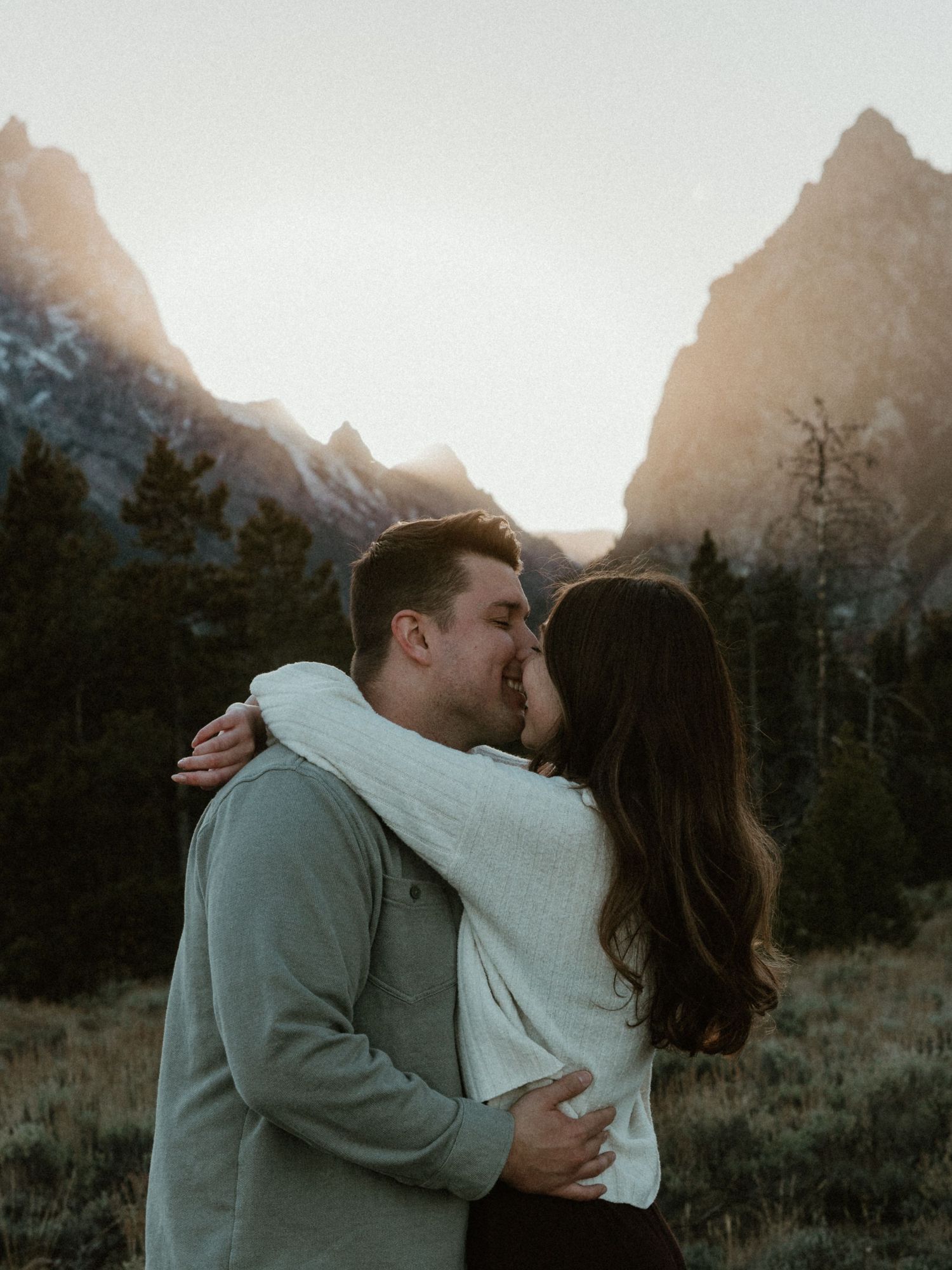 Intimate embrace captured against snow-capped mountain peaks during golden hour.