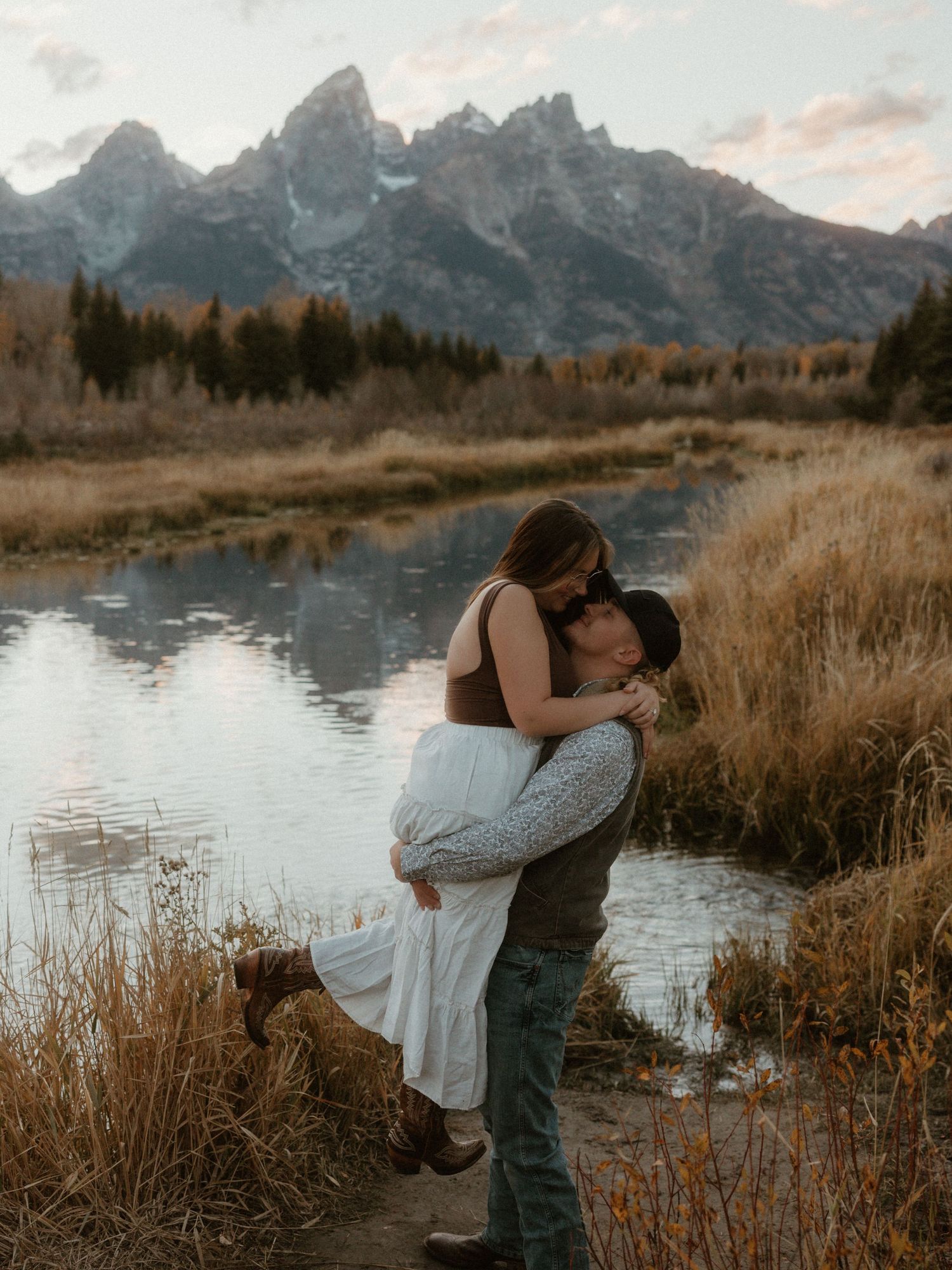 Couple sharing an intimate embrace by a scenic mountain lake during sunset.