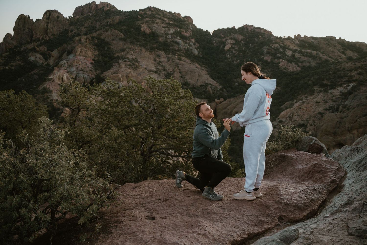 Two people sit on a rugged mountain overlook during golden hour.