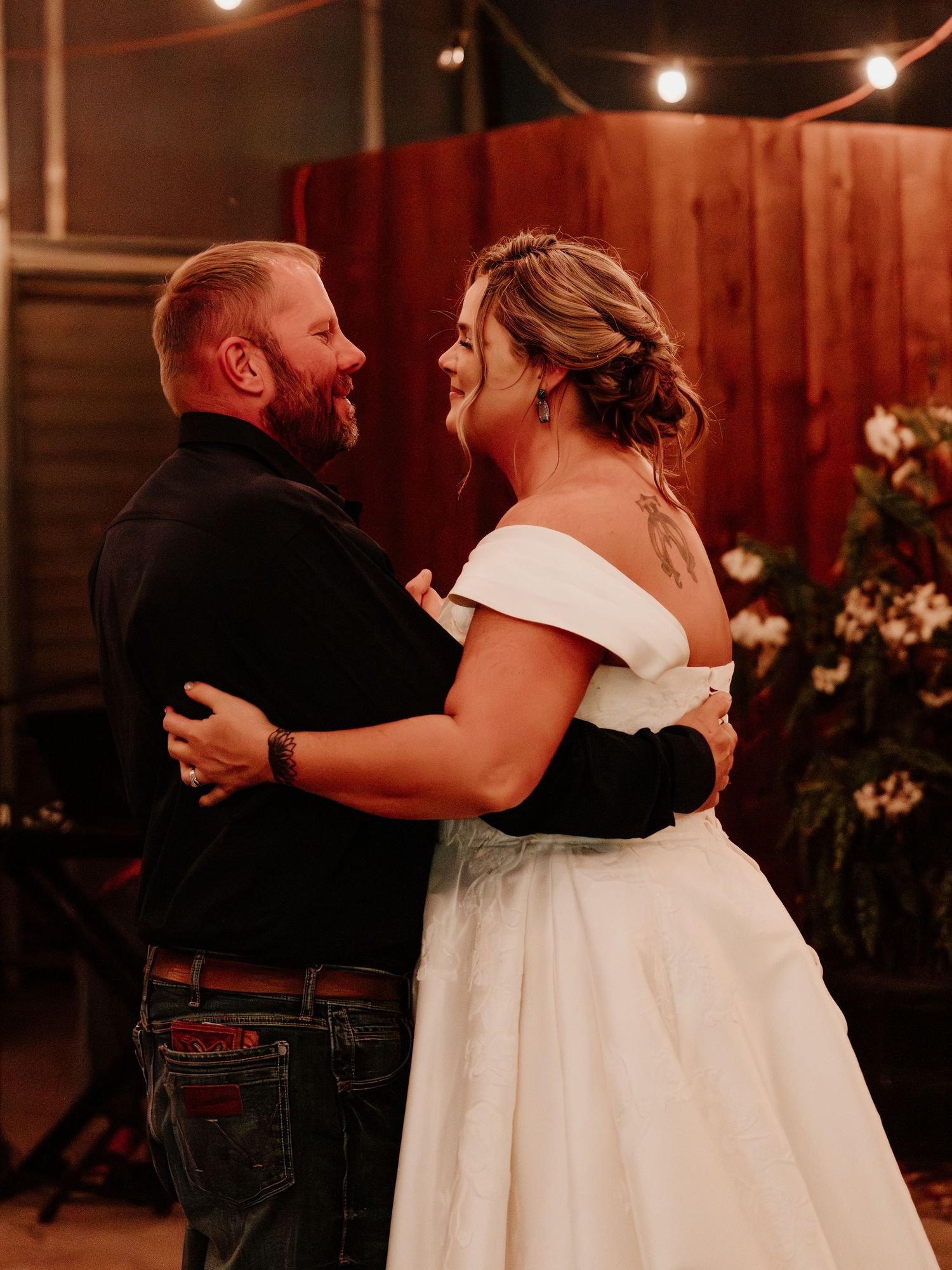 A couple shares a joyful dance moment at their wedding reception with wooden paneling and string lights in the background.