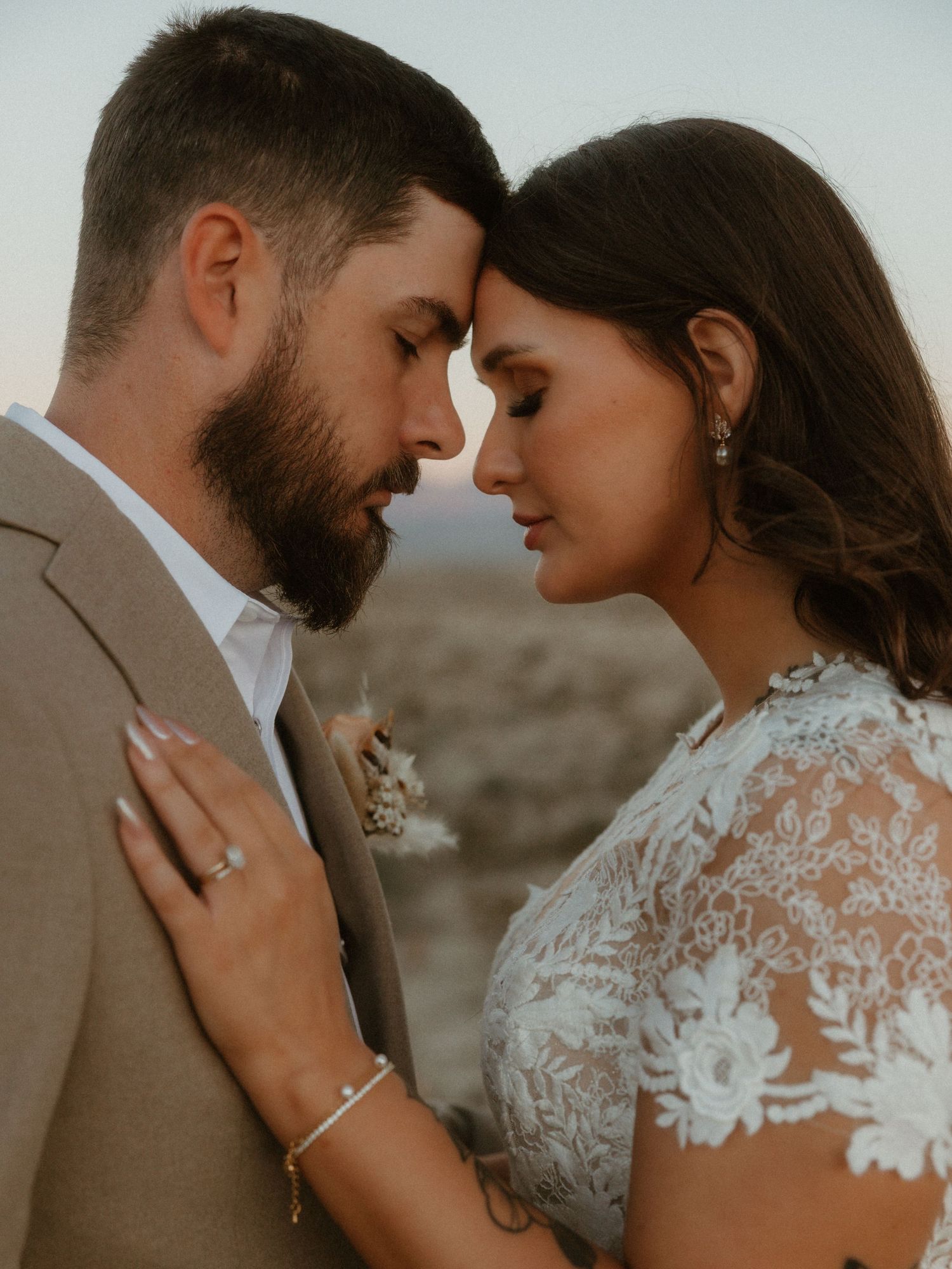 Intimate wedding portrait of couple in romantic pose against desert backdrop.