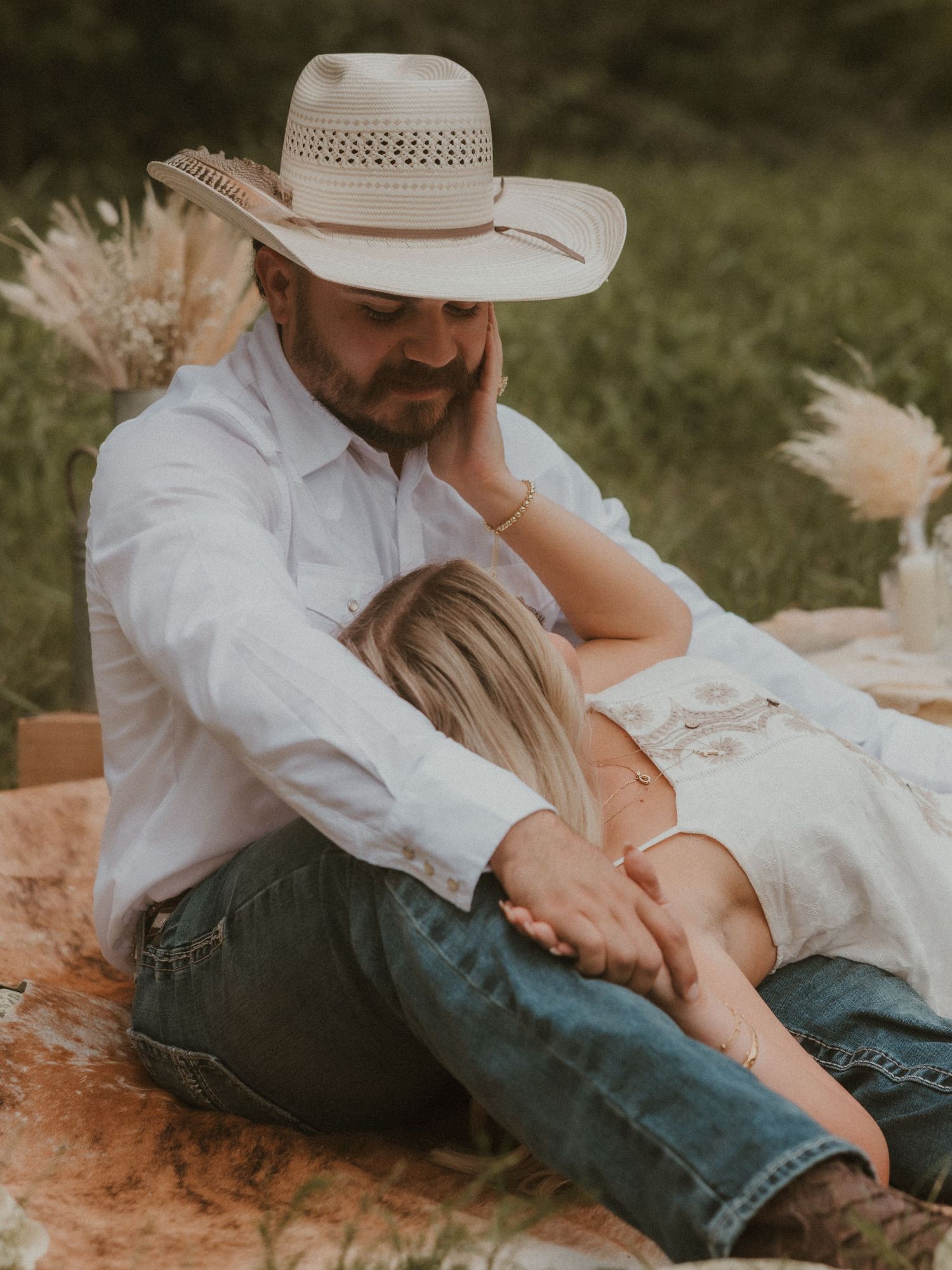 Intimate countryside photoshoot featuring couple in western attire relaxing on grass.