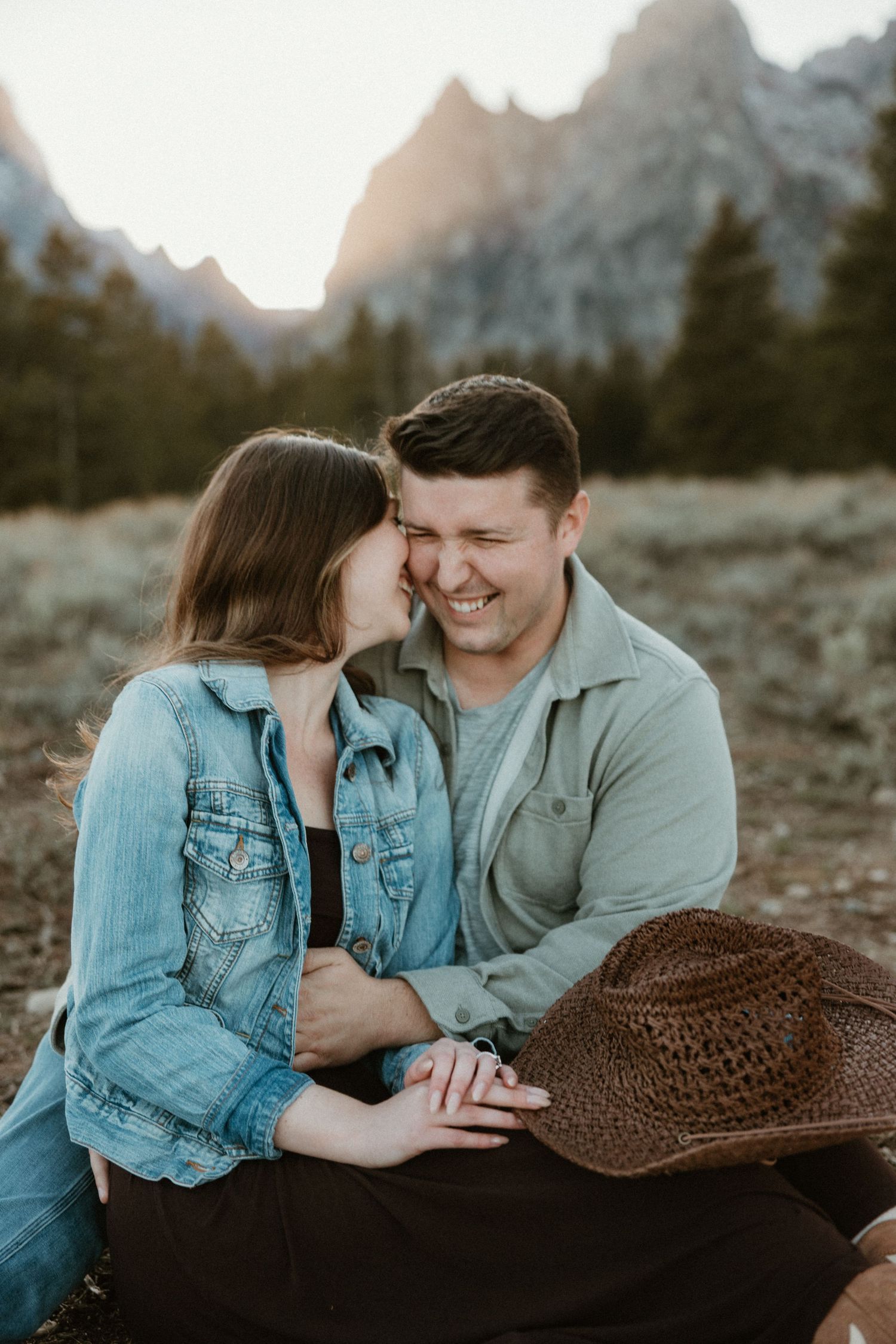 Intimate moment shared between couple with straw hat against mountain backdrop.