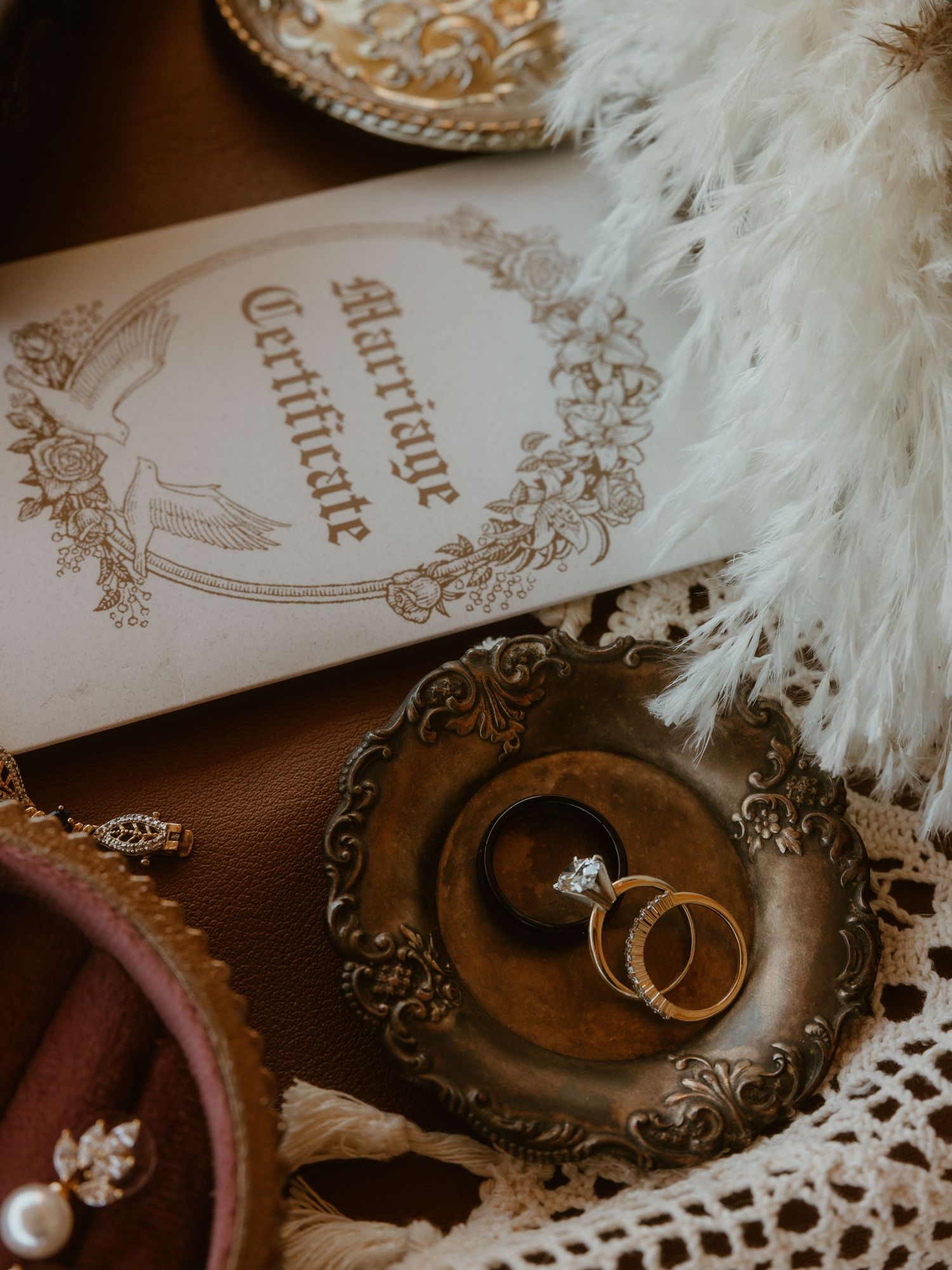 Wedding rings rest on vintage lace and paper with delicate white feather accents in a romantic arrangement.